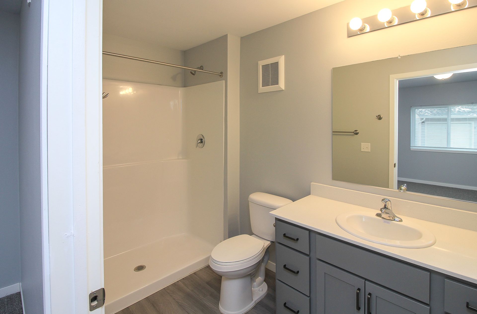 Modern bathroom with walk-in shower, white toilet, gray vanity, and large mirror.