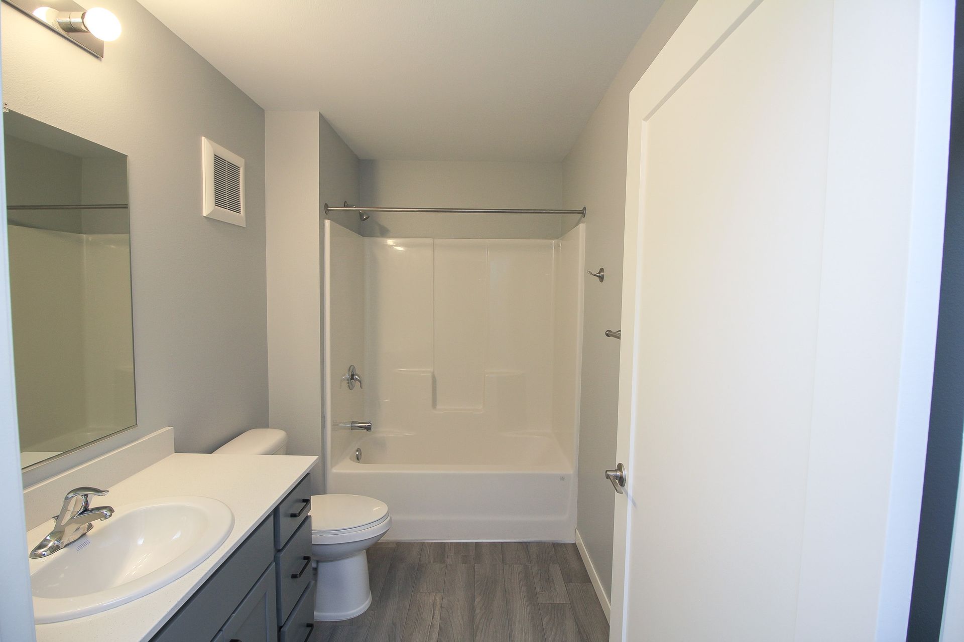 Bathroom with white tub and shower, toilet, sink vanity, and gray walls and flooring.