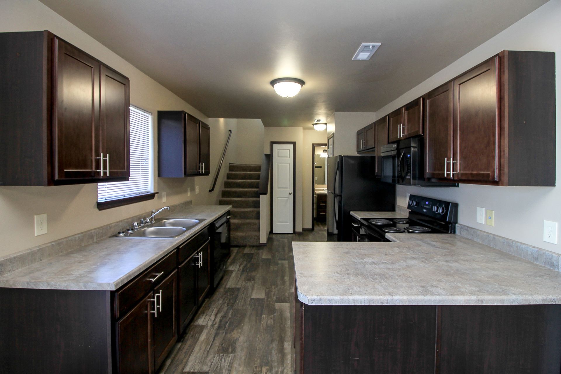 Modern kitchen with dark wood cabinets, gray countertops, and stainless appliances, viewed from the center.
