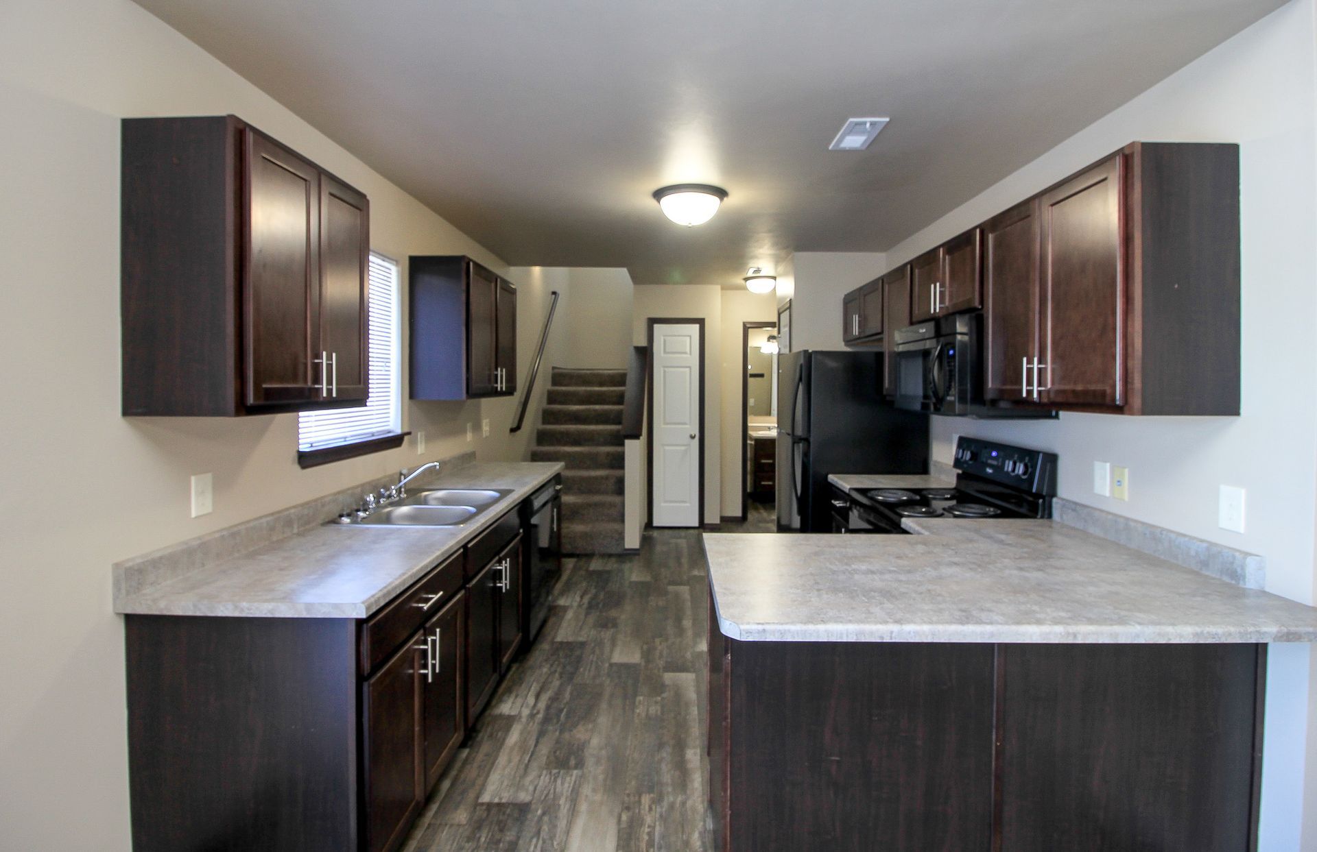 Modern kitchen with dark wood cabinets, light countertops, island, stainless appliances, and tiled floor