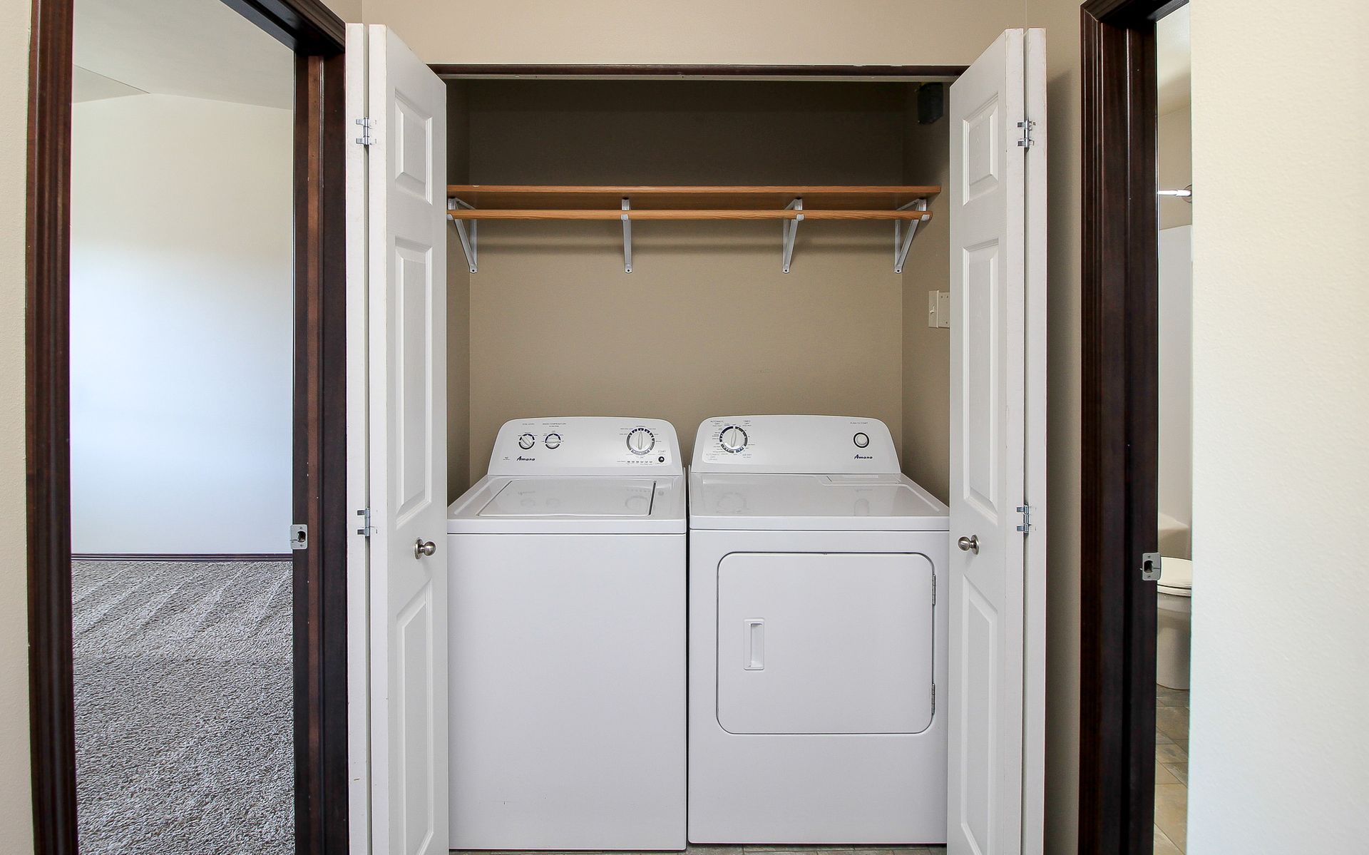 Laundry closet with a white washer and dryer under a shelf and hanging rod, behind open doors
