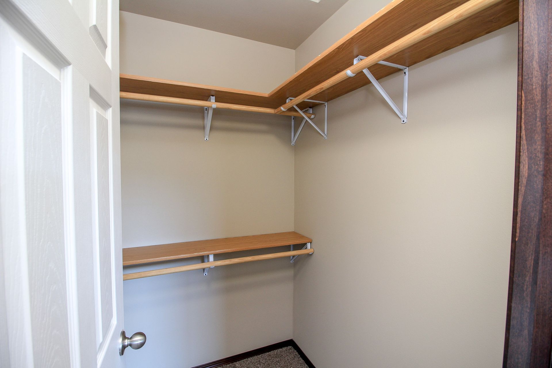 Empty walk-in closet with white walls, wood shelves, and hanging rods.