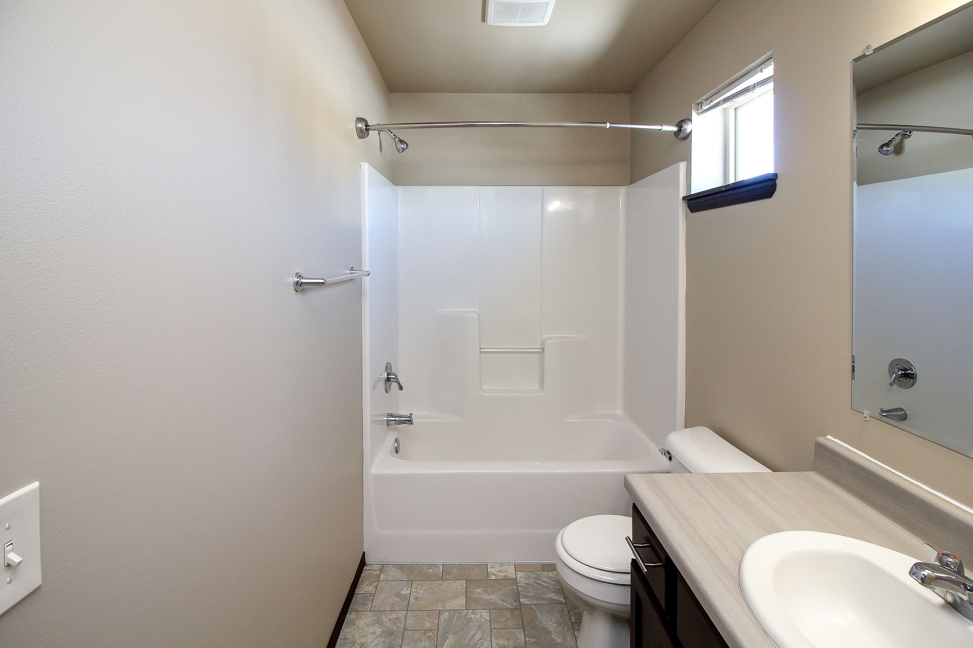 Bathroom with white tub-shower, toilet, sink vanity, mirror, and small window.