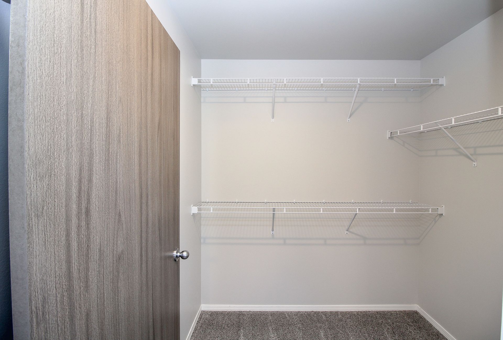 Empty walk-in closet with white wire shelves and hanging rods beside a wood-paneled door.
