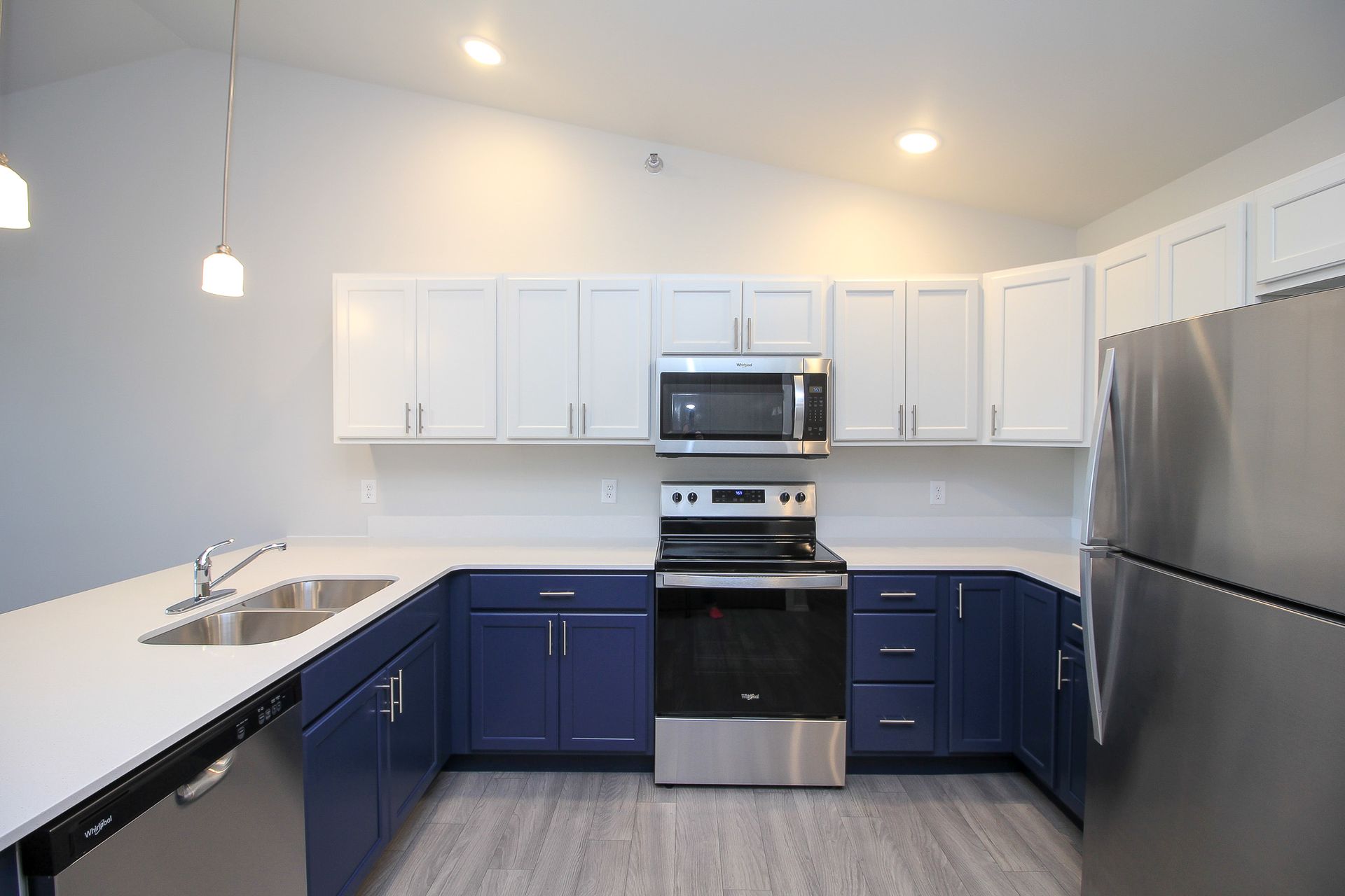 Modern kitchen with white upper cabinets, navy lower cabinets, stainless appliances, and a large island counter