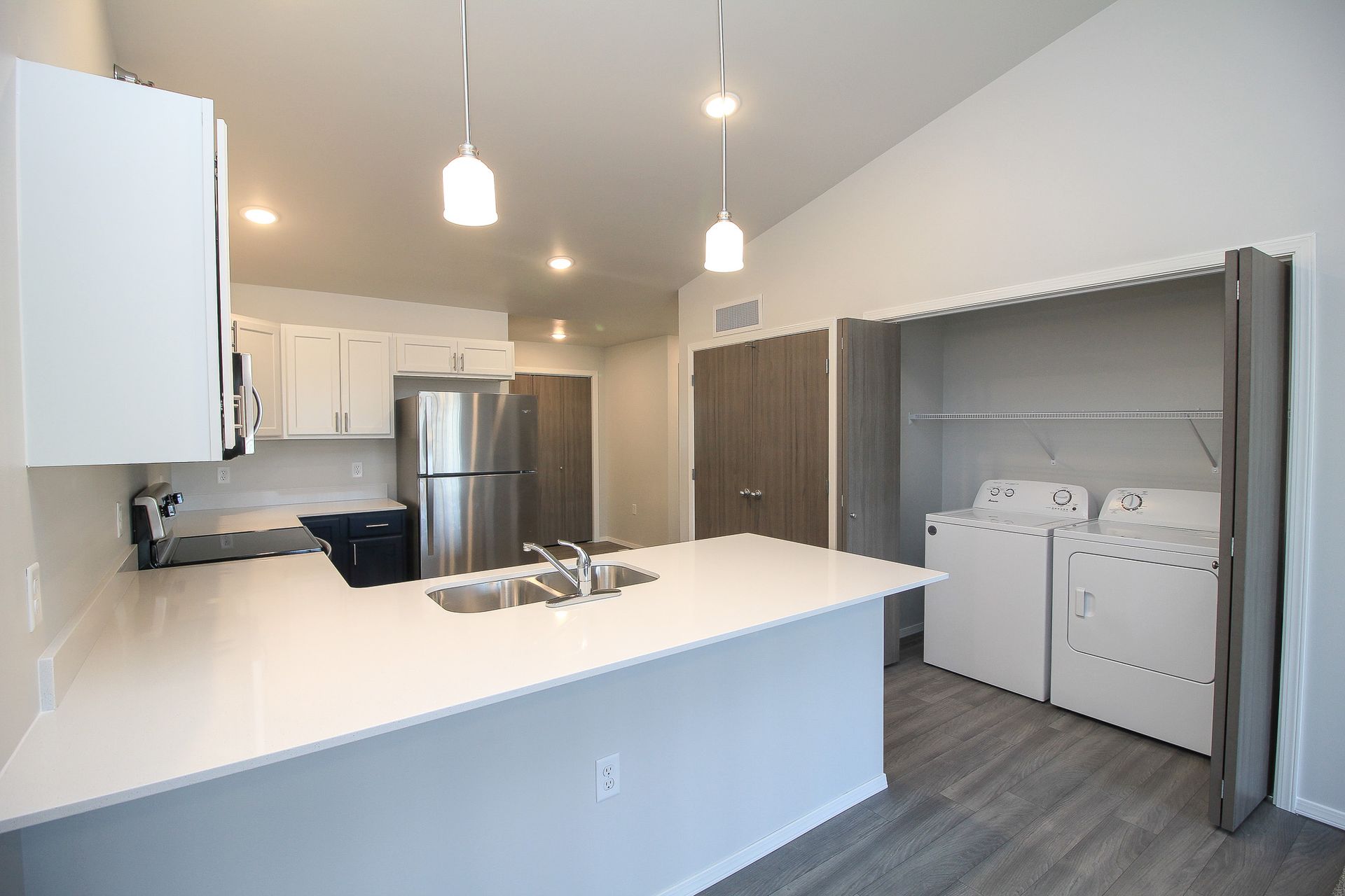 Bright modern kitchen with white cabinets, stainless fridge, island, and laundry nook with washer and dryer.
