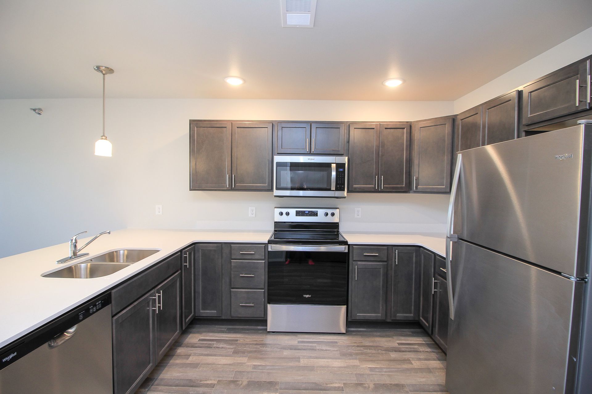 Modern kitchen with dark cabinets, stainless steel appliances, white countertops, and a large island sink