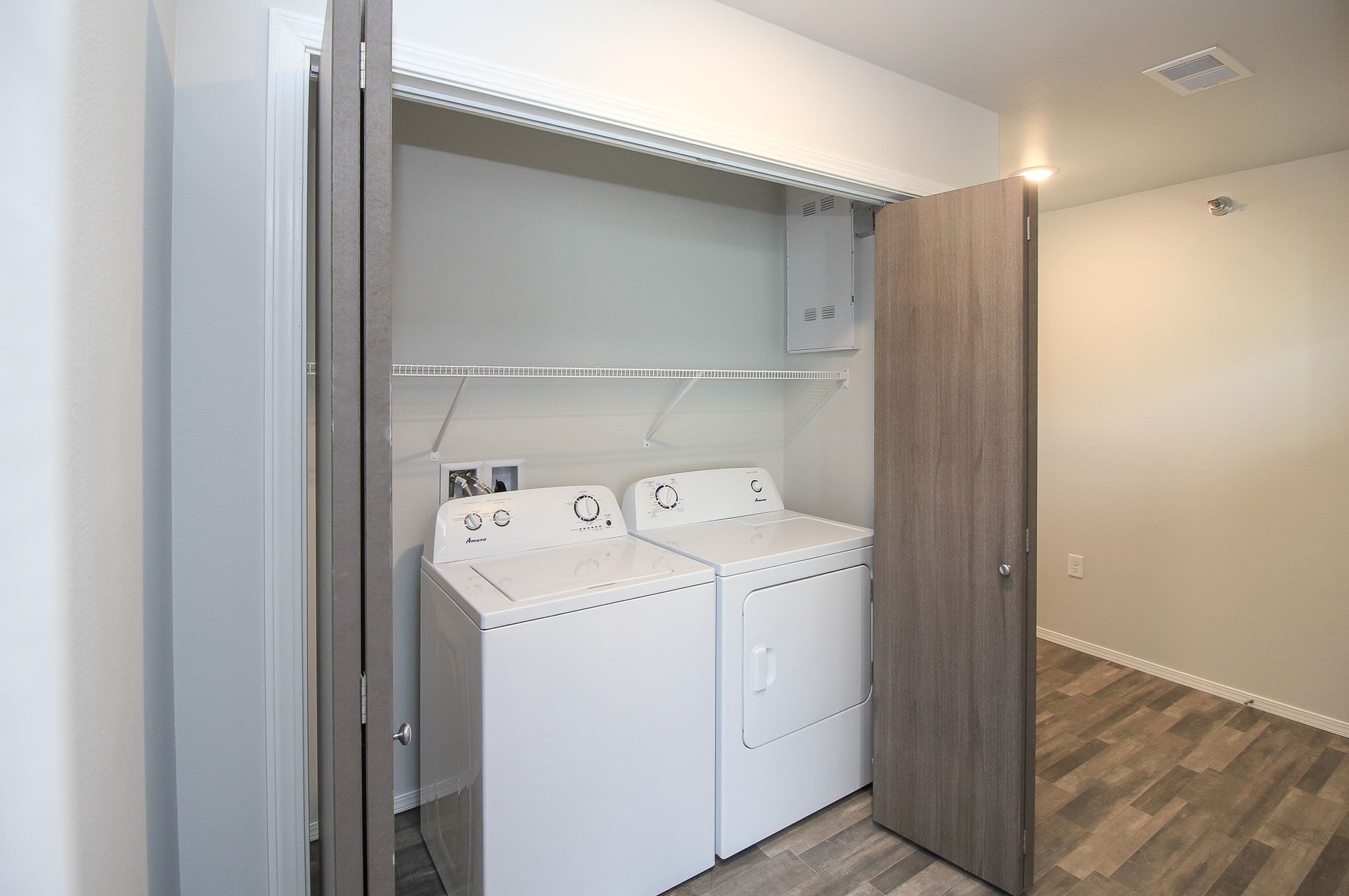 Laundry closet with washer and dryer behind open sliding doors in a hallway.