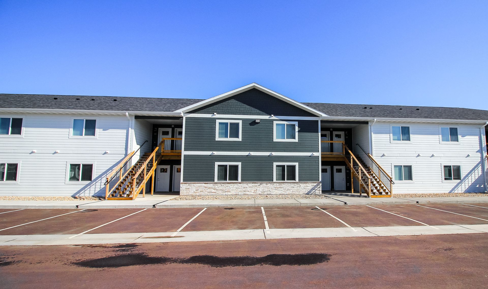 Apartment building with central gray section, white wings, and front stairs under a clear blue sky