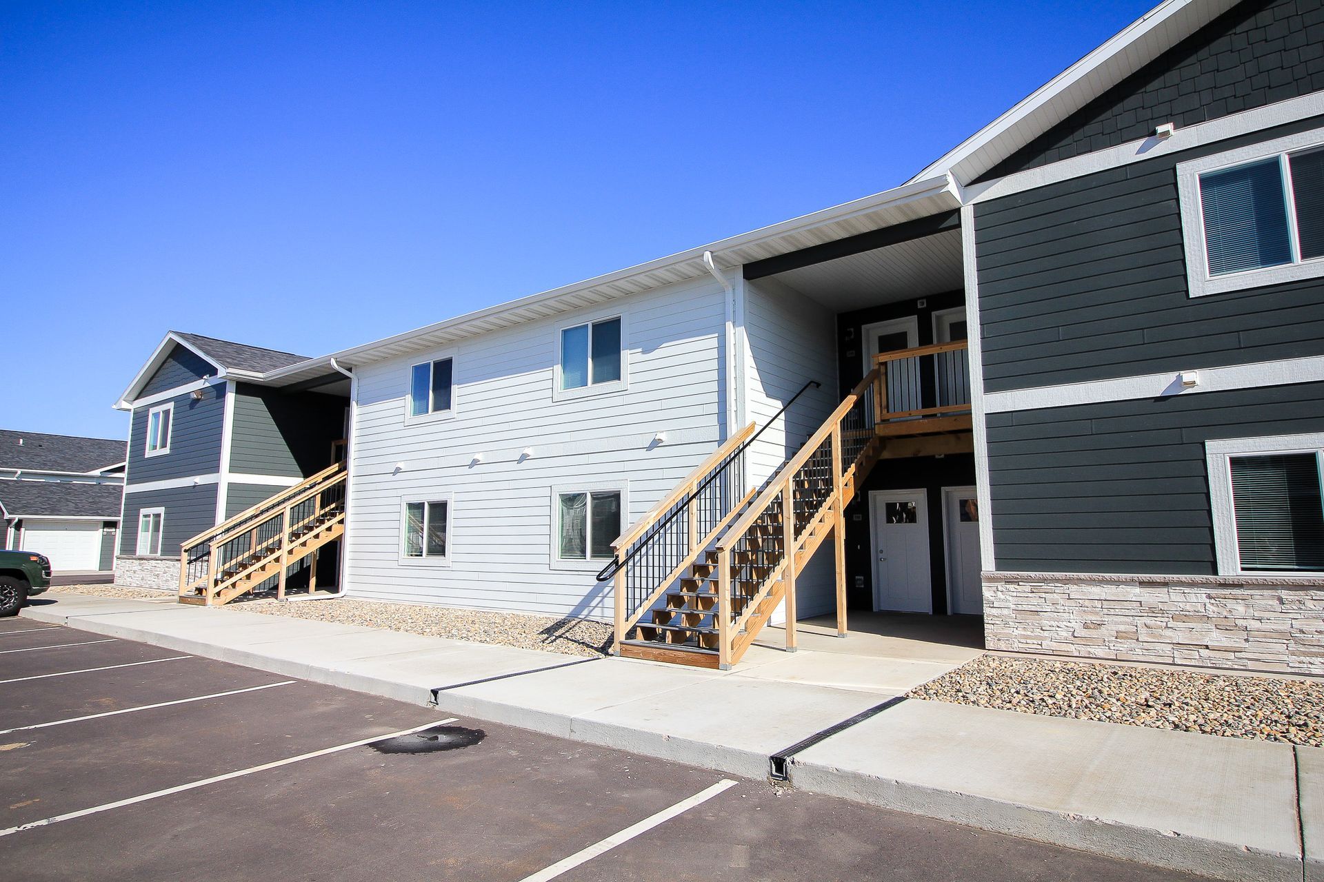 Row of blue and gray apartment buildings with exterior stairways and a parking lot under a clear sky