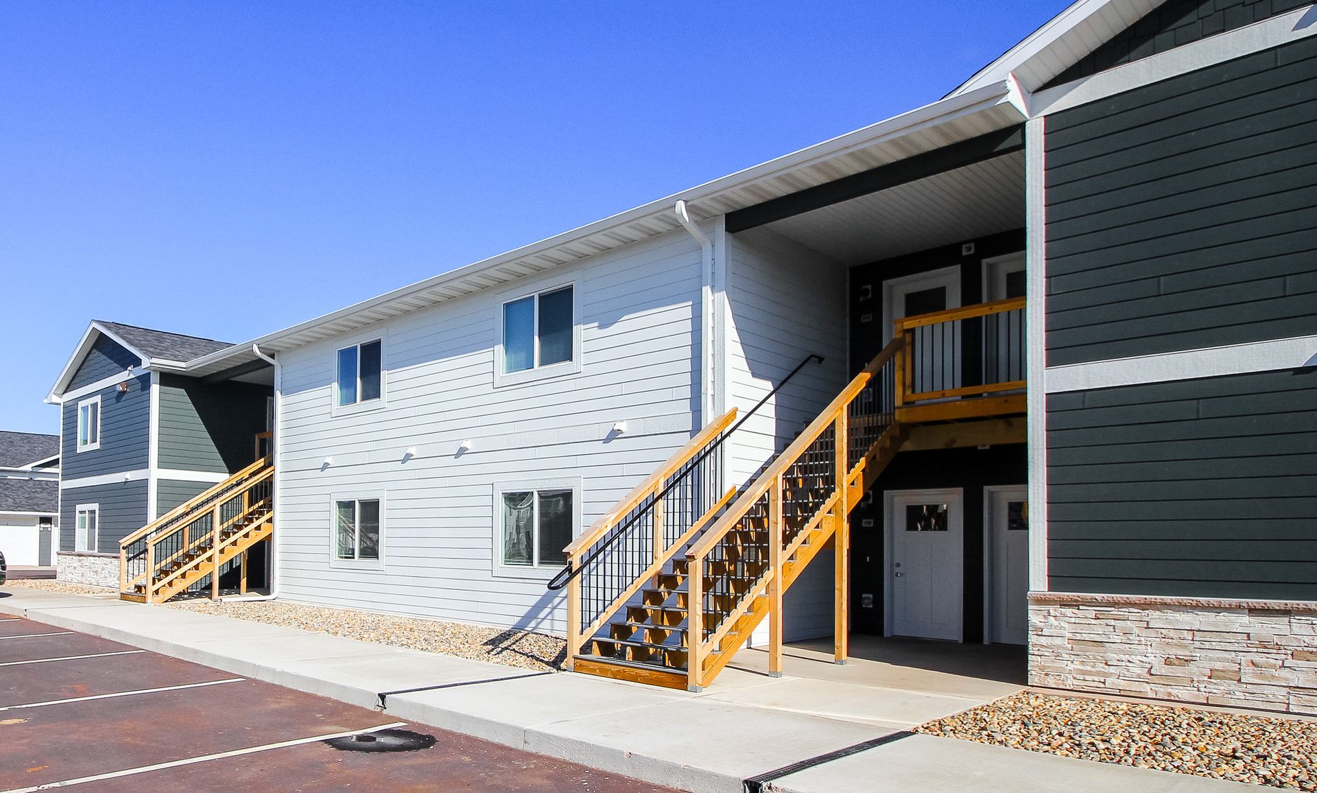 Modern apartment building exterior with white and dark gray siding, yellow stair railings, and blue sky