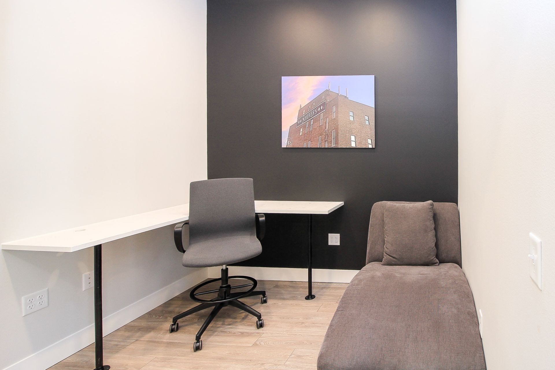 Small office nook with desk, gray chair, brown bench, and mountain photo on a dark accent wall.