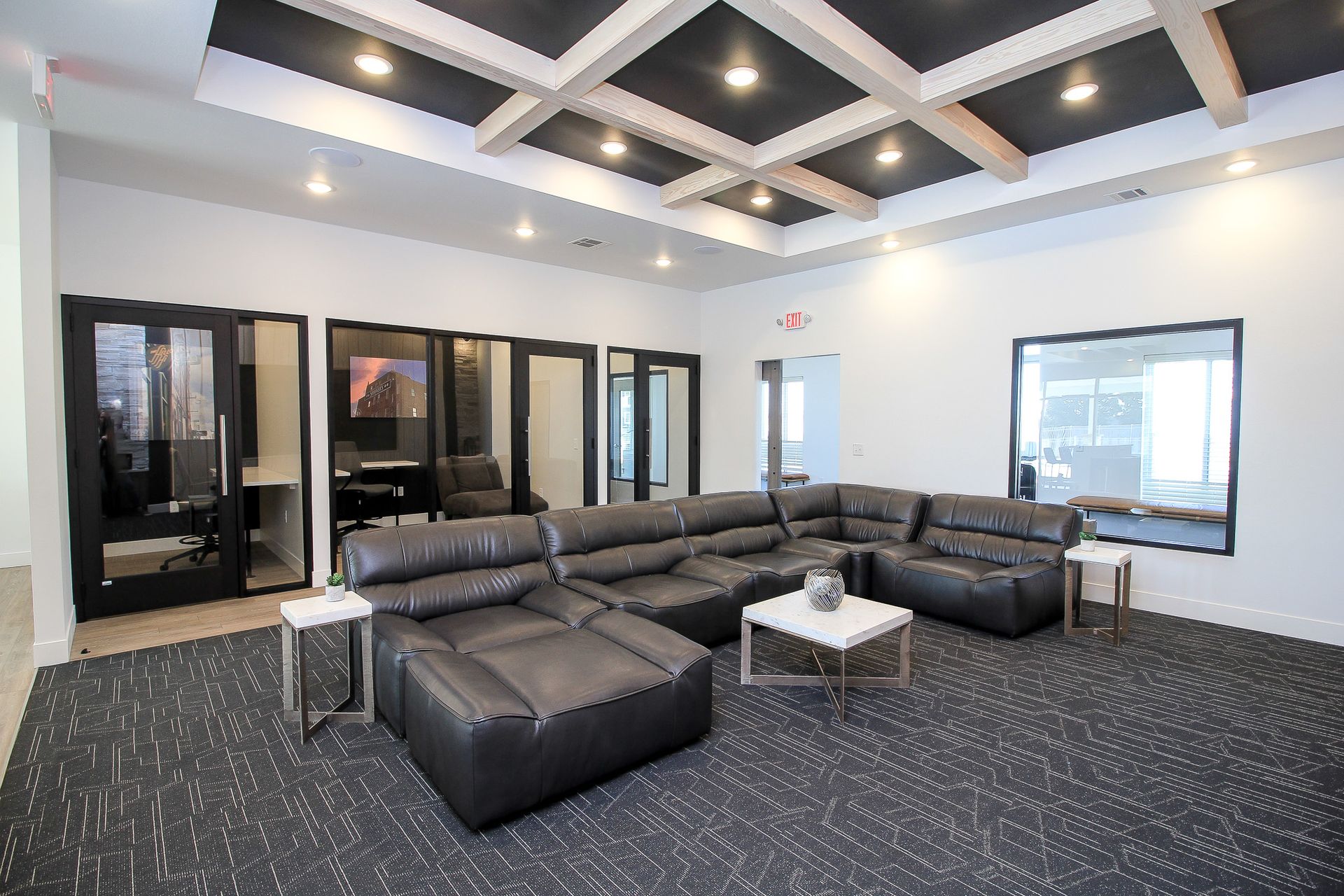 Modern lounge with black sectional sofa, coffee tables, and a coffered ceiling in a bright office lobby
