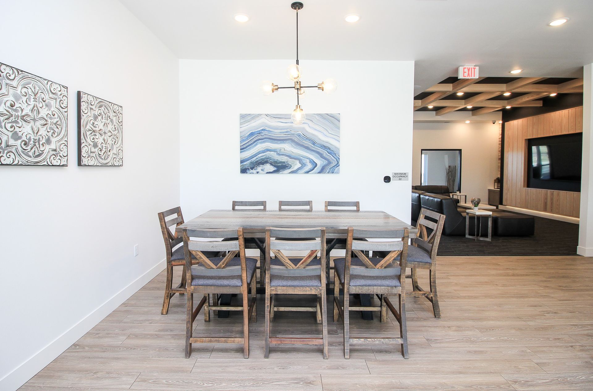 Modern dining room with wooden table, chairs, and abstract wall art, opening to a living area.