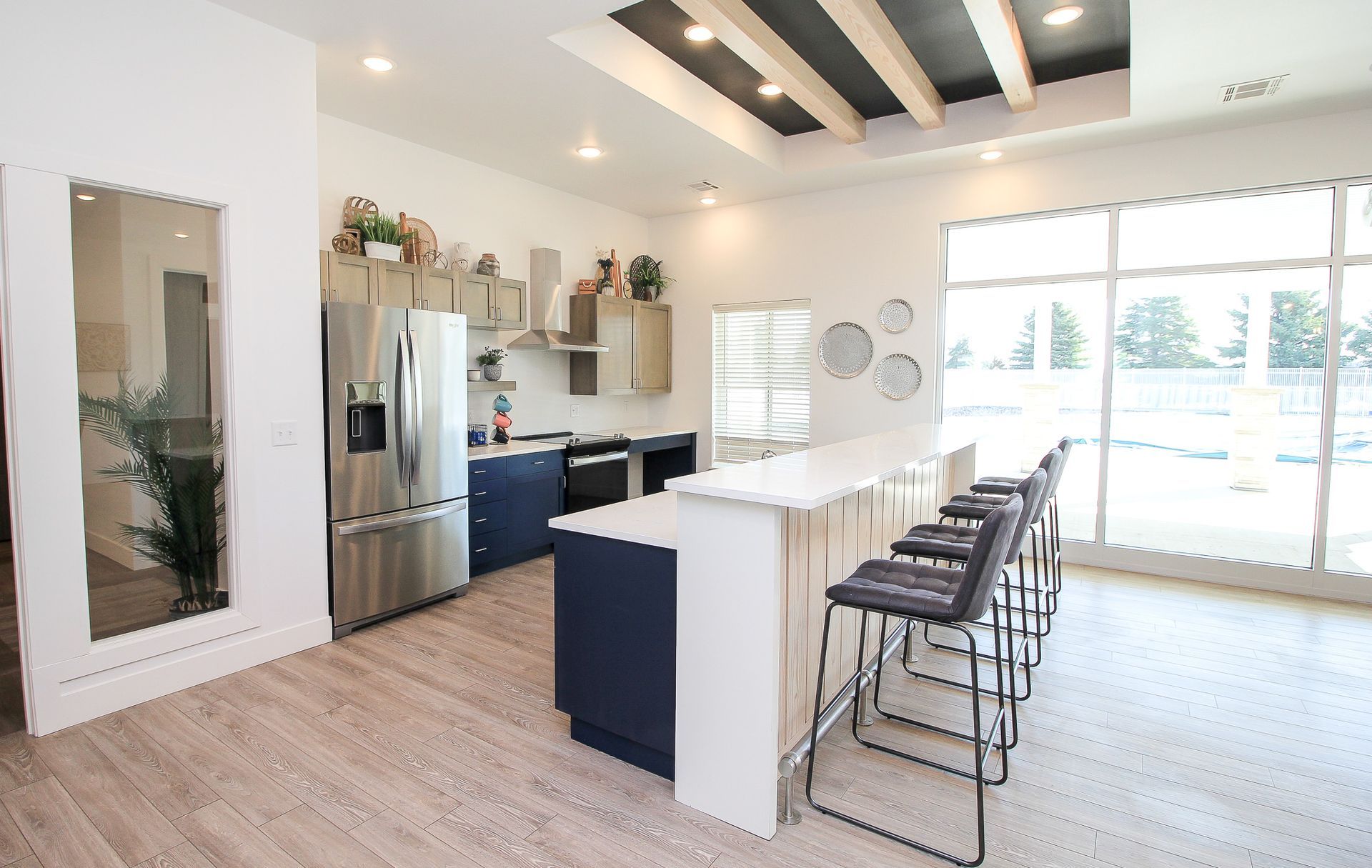 Bright modern kitchen with white island, bar stools, stainless fridge, and large sliding glass doors
