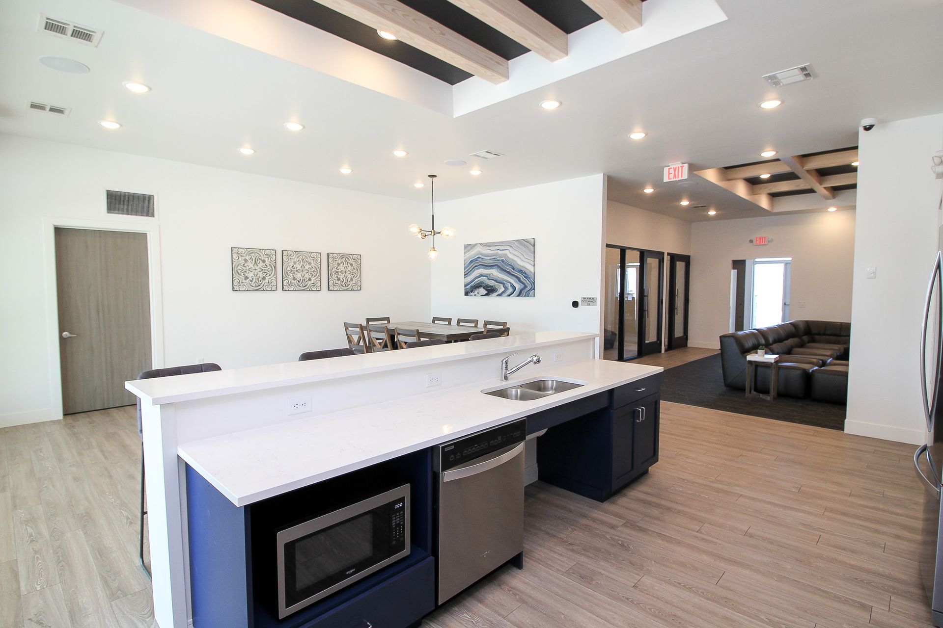 Modern open-plan kitchen and living area with white island, wood floors, and dark sofa seating