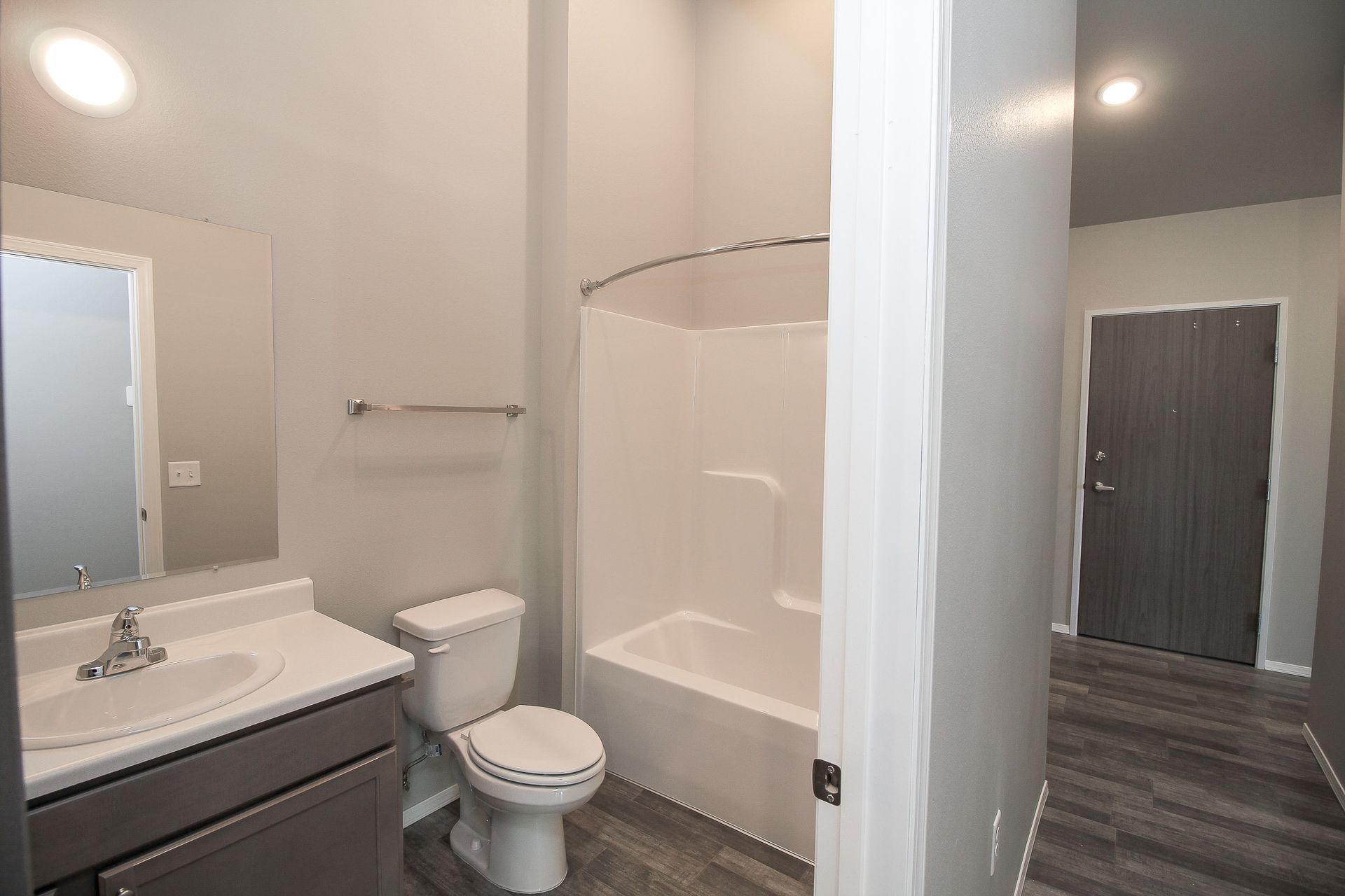 Small bathroom with white tub, toilet, sink vanity, and mirror on beige walls.