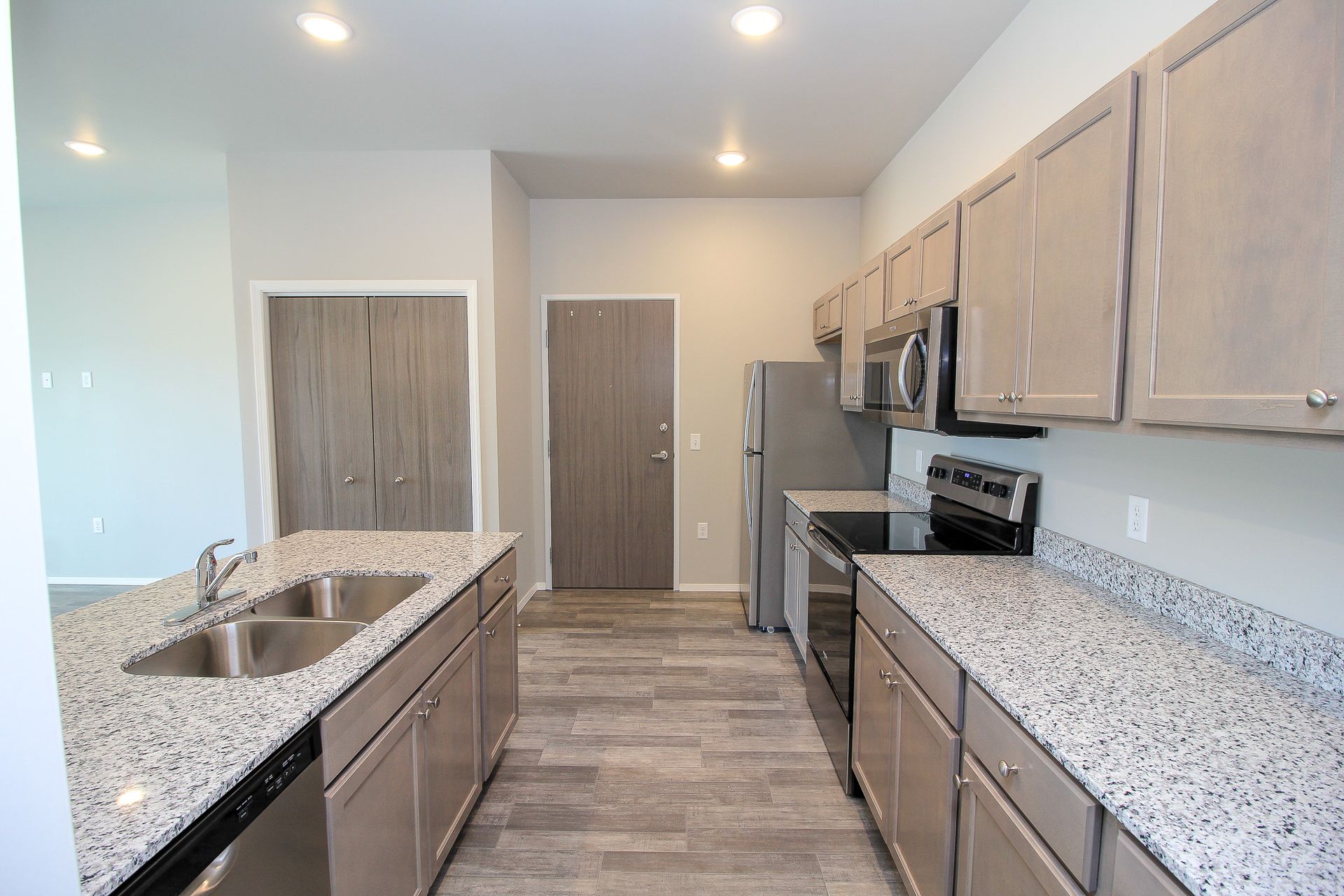 Modern kitchen with light wood cabinets, speckled granite counters, stainless appliances, and gray wood-look flooring
