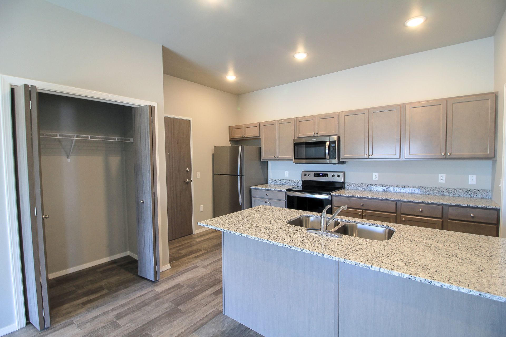 Modern kitchen with granite island, stainless appliances, gray cabinets, and a closet opening on the left