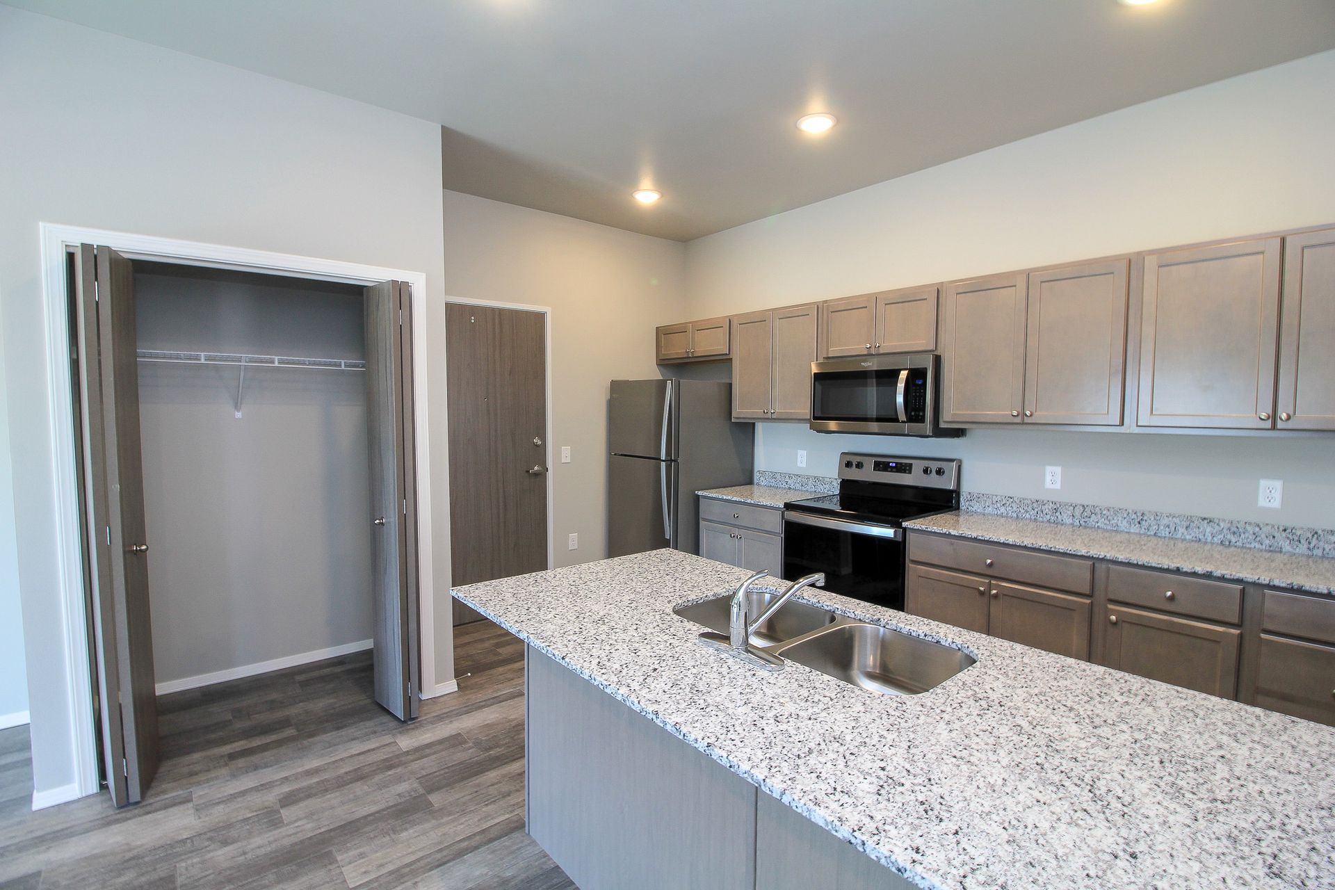 Modern kitchen with granite island, stainless appliances, and open pantry closet