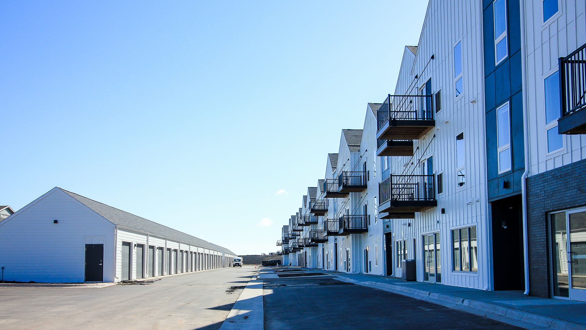 Industrial street with white buildings and balconies along a paved road under a clear blue sky