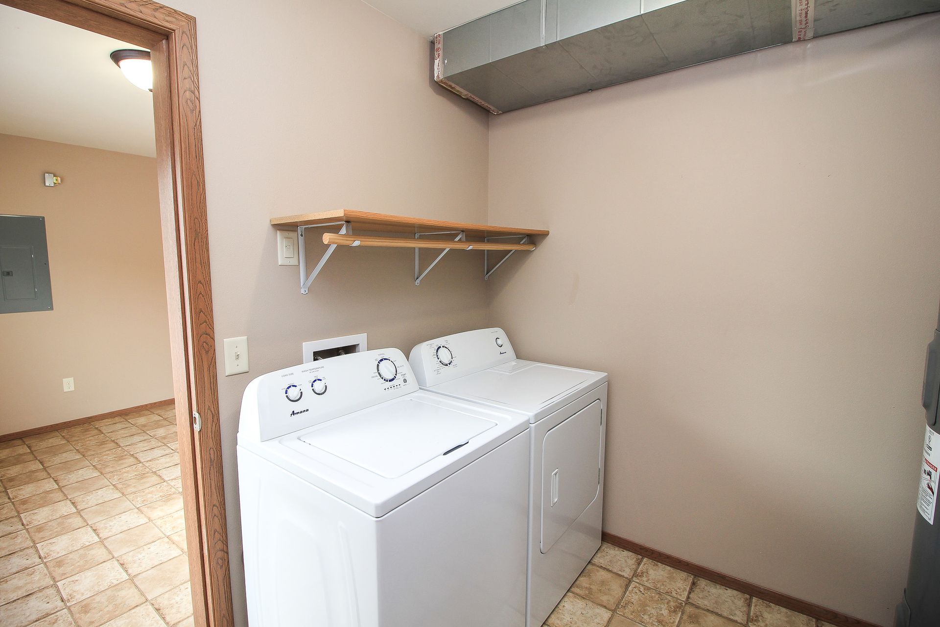 Laundry room with a white washer and dryer, wall shelf, and tiled floor.