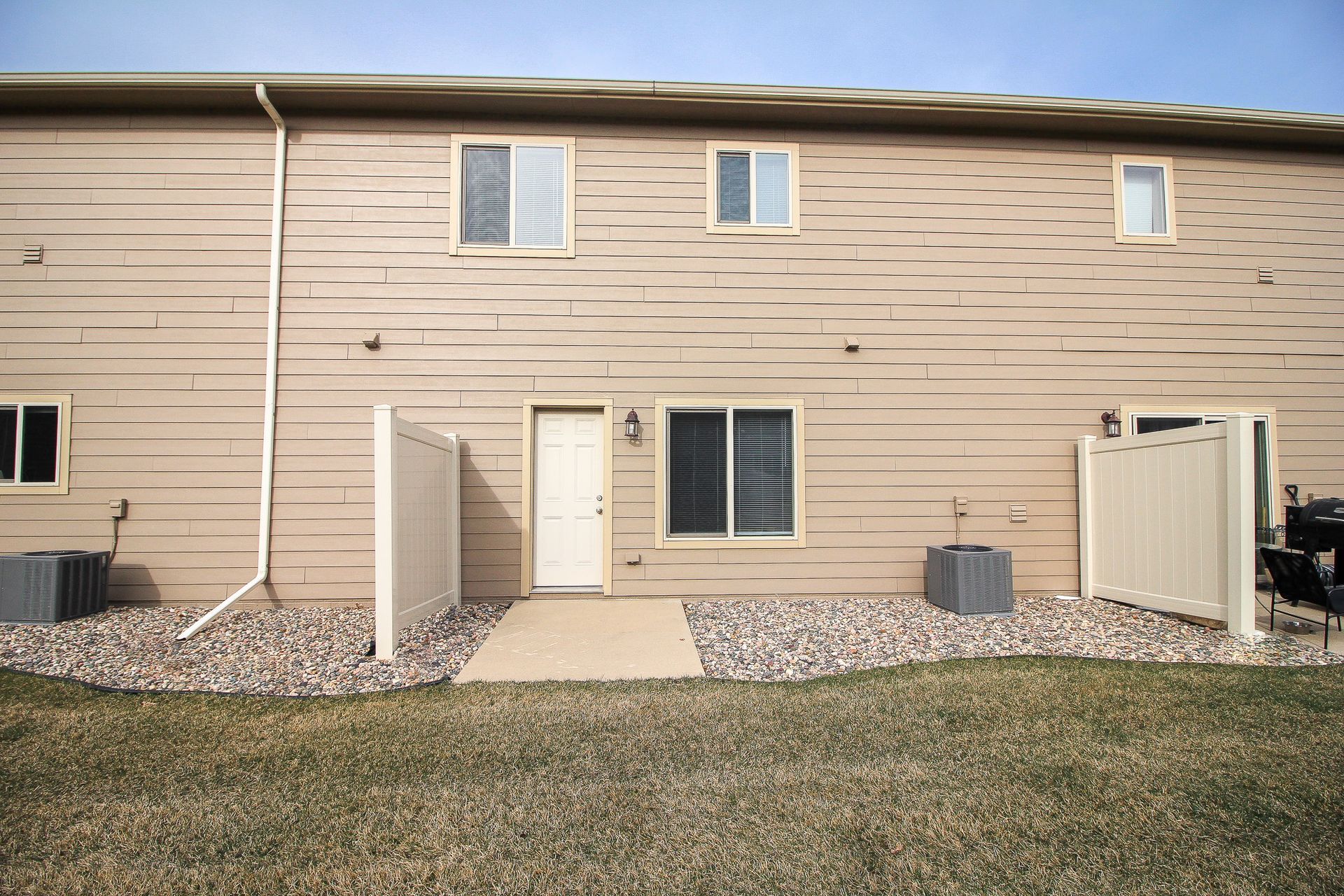 Tan townhouse row with beige siding, small front patio, and grassy yard under overcast sky