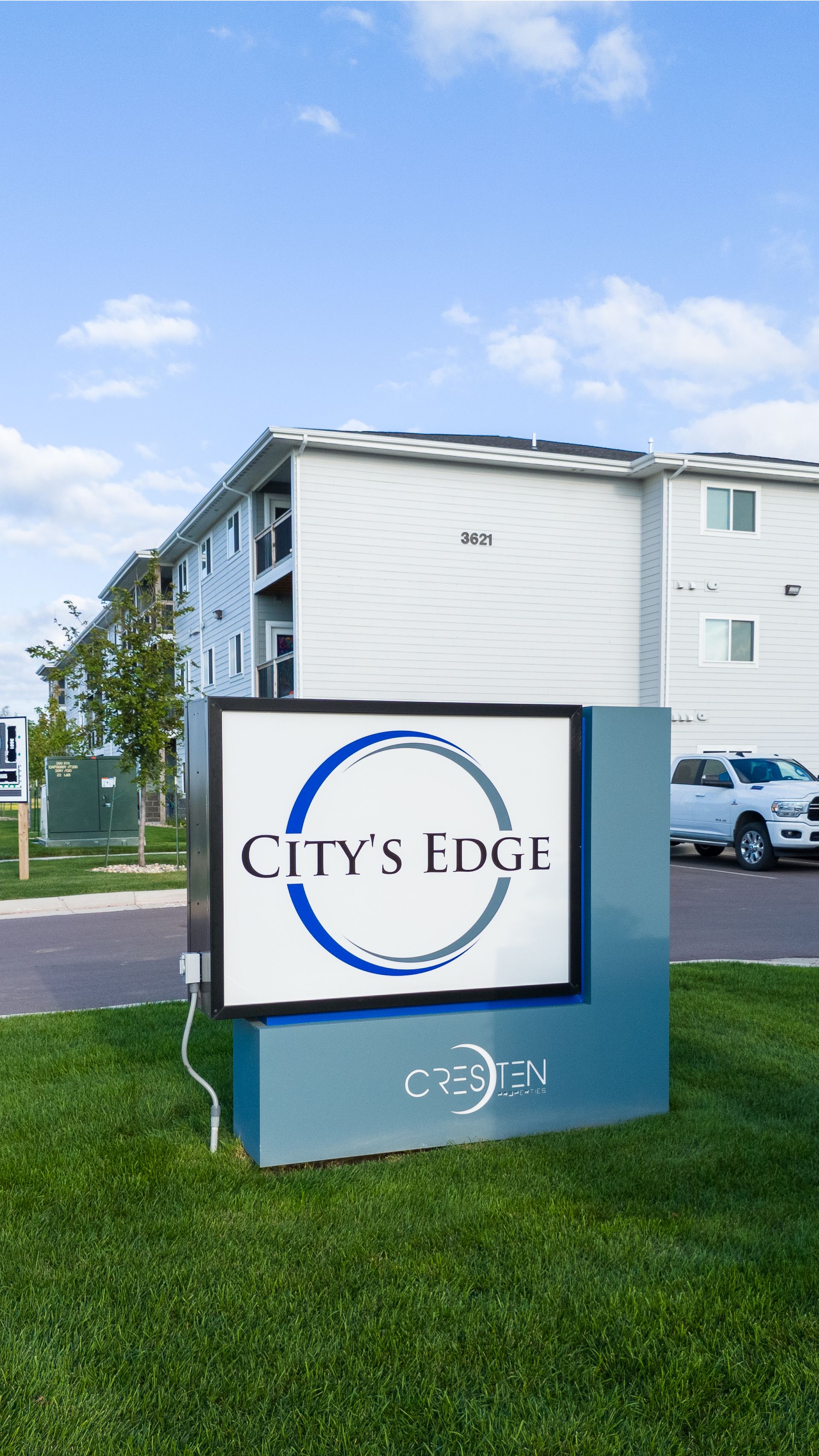 City’s Edge apartment sign on a grassy lawn with buildings and parked cars in the background