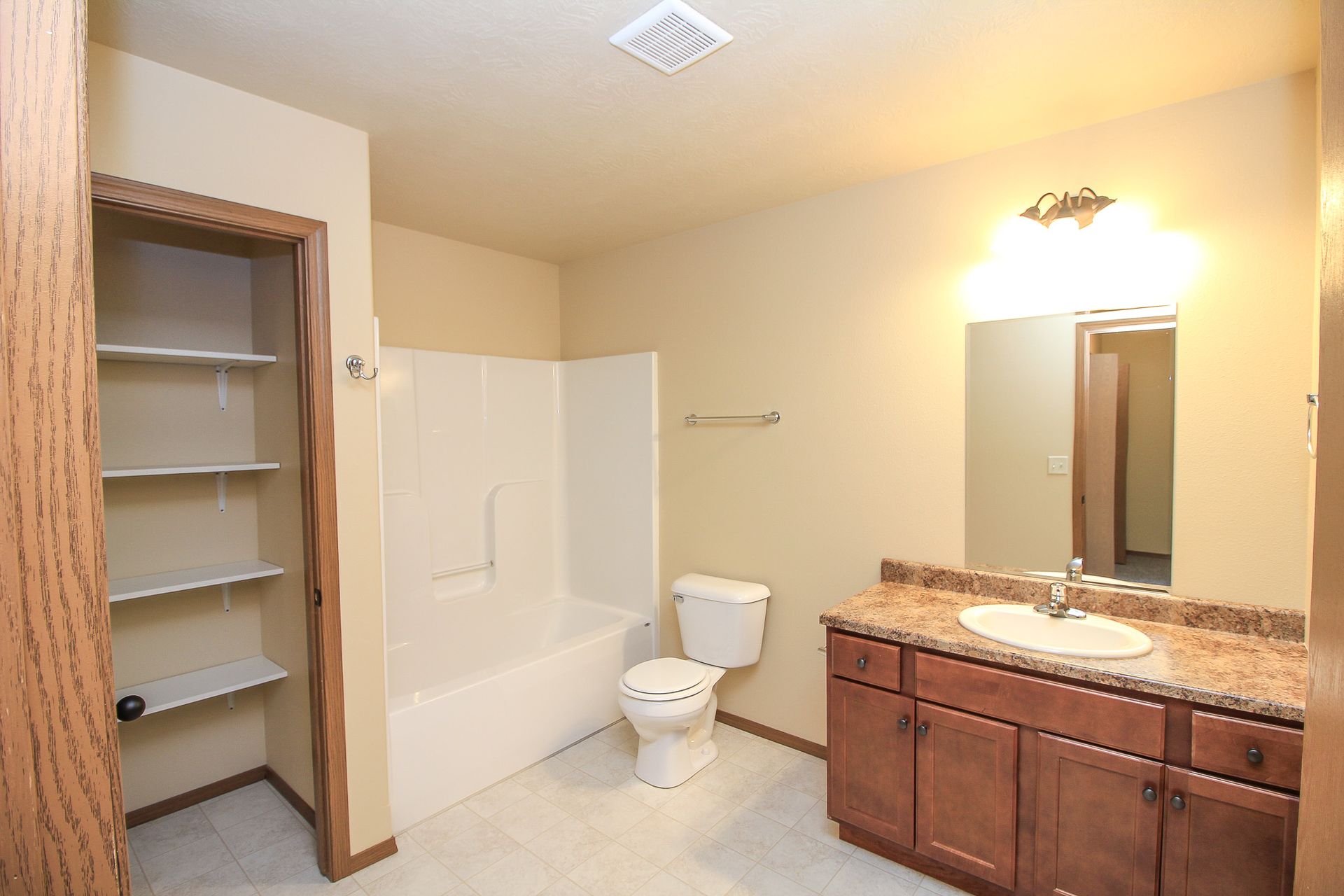 Bathroom with tub, toilet, and wood vanity with granite countertop, viewed from the doorway