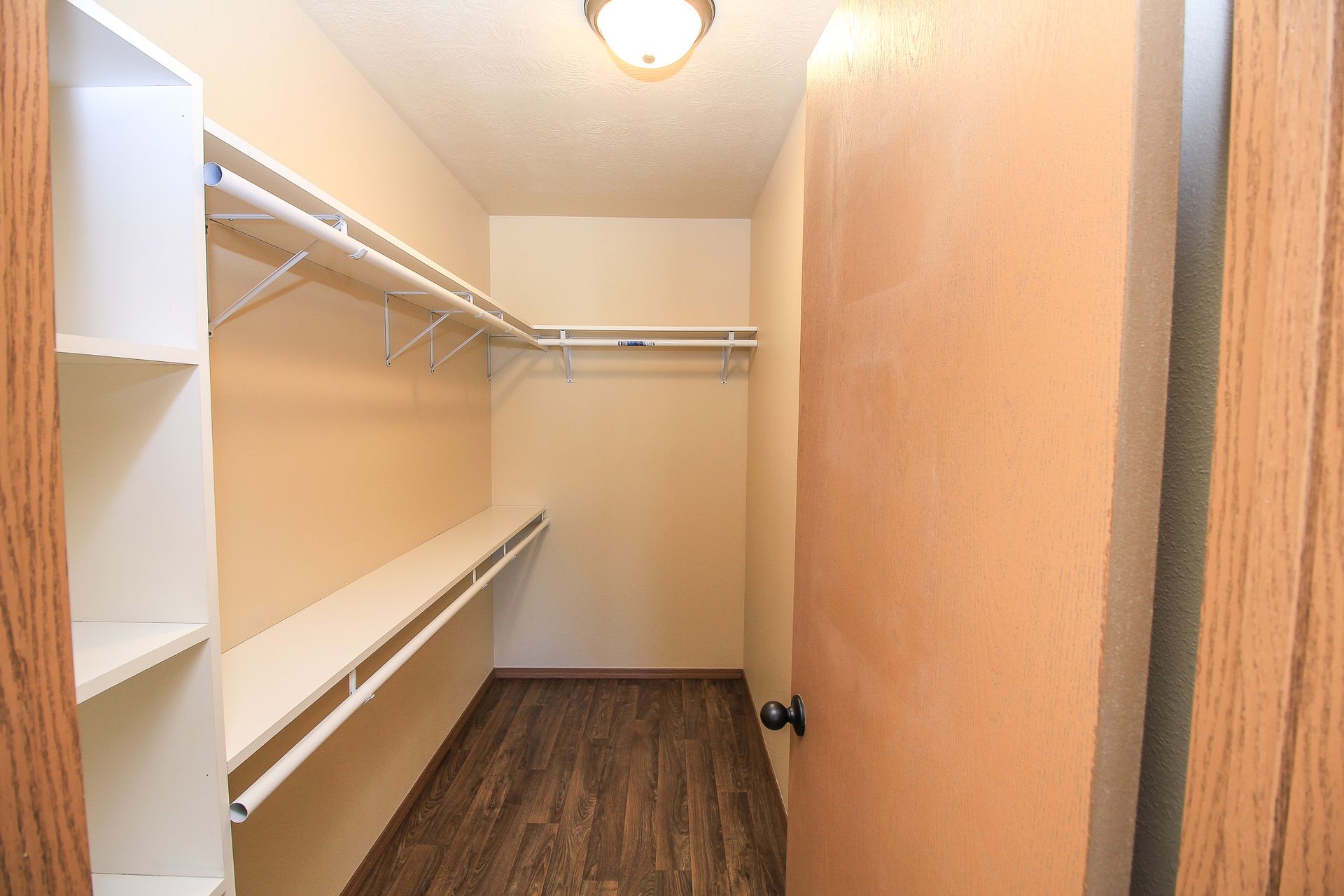 Empty walk-in closet with white shelves, hanging rods, and wood flooring