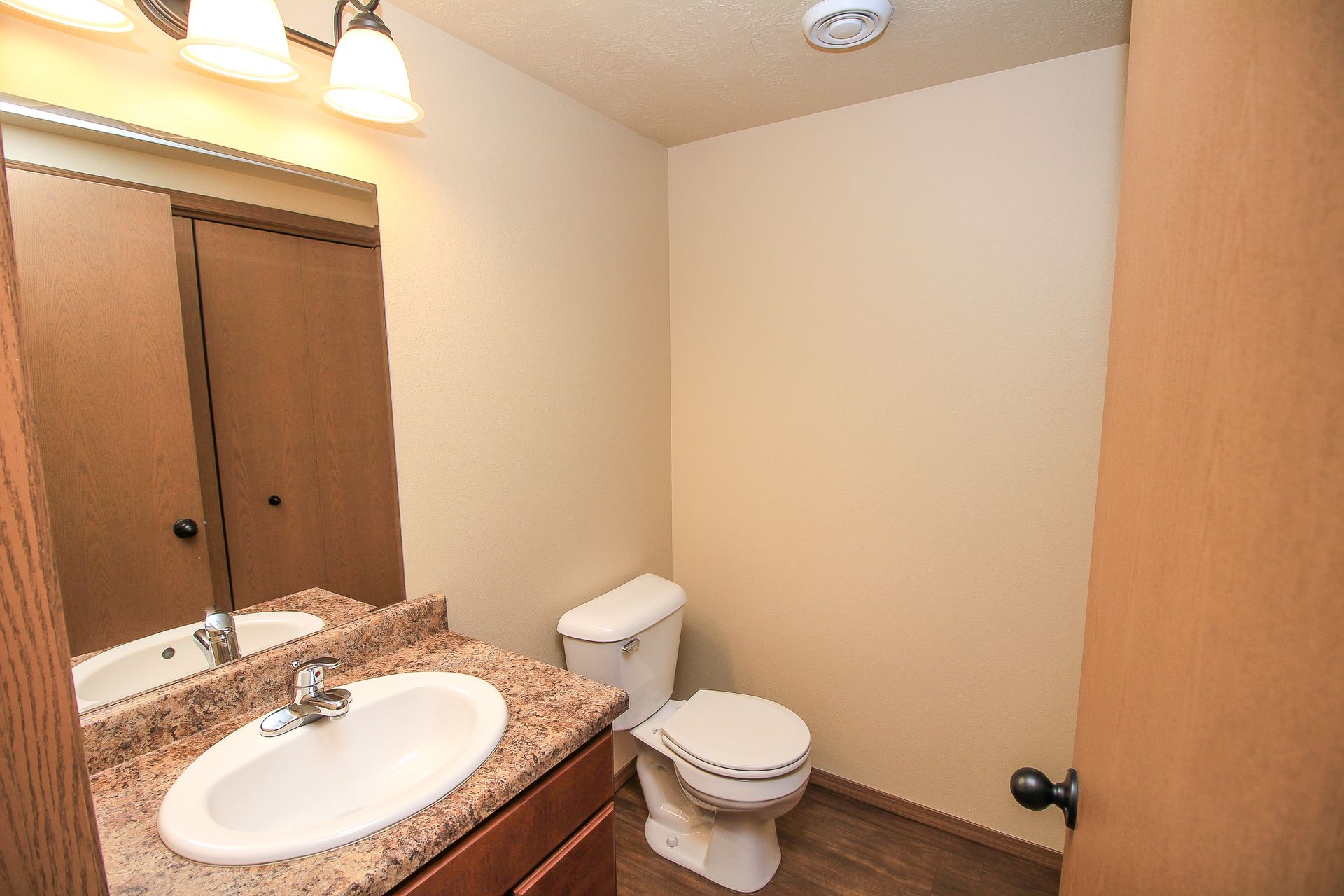 Small bathroom with sink, mirror, toilet, and wooden cabinet doors in beige tones.