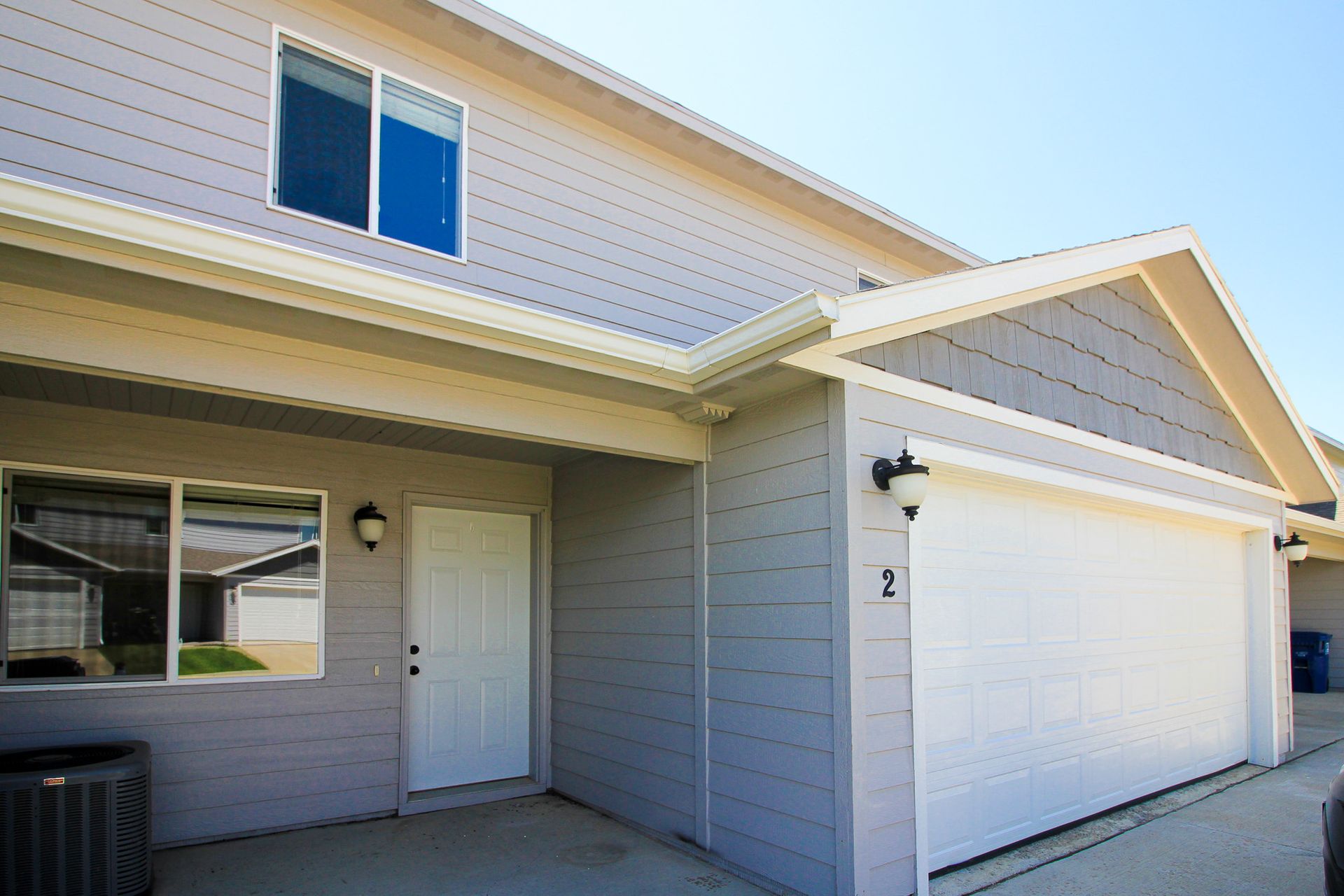 Exterior of a gray house with white garage and front door, seen from the driveway