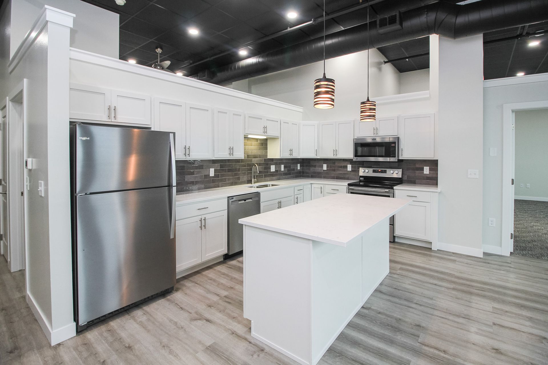 Modern kitchen with stainless steel appliances, white cabinets, and gray tile backsplash.