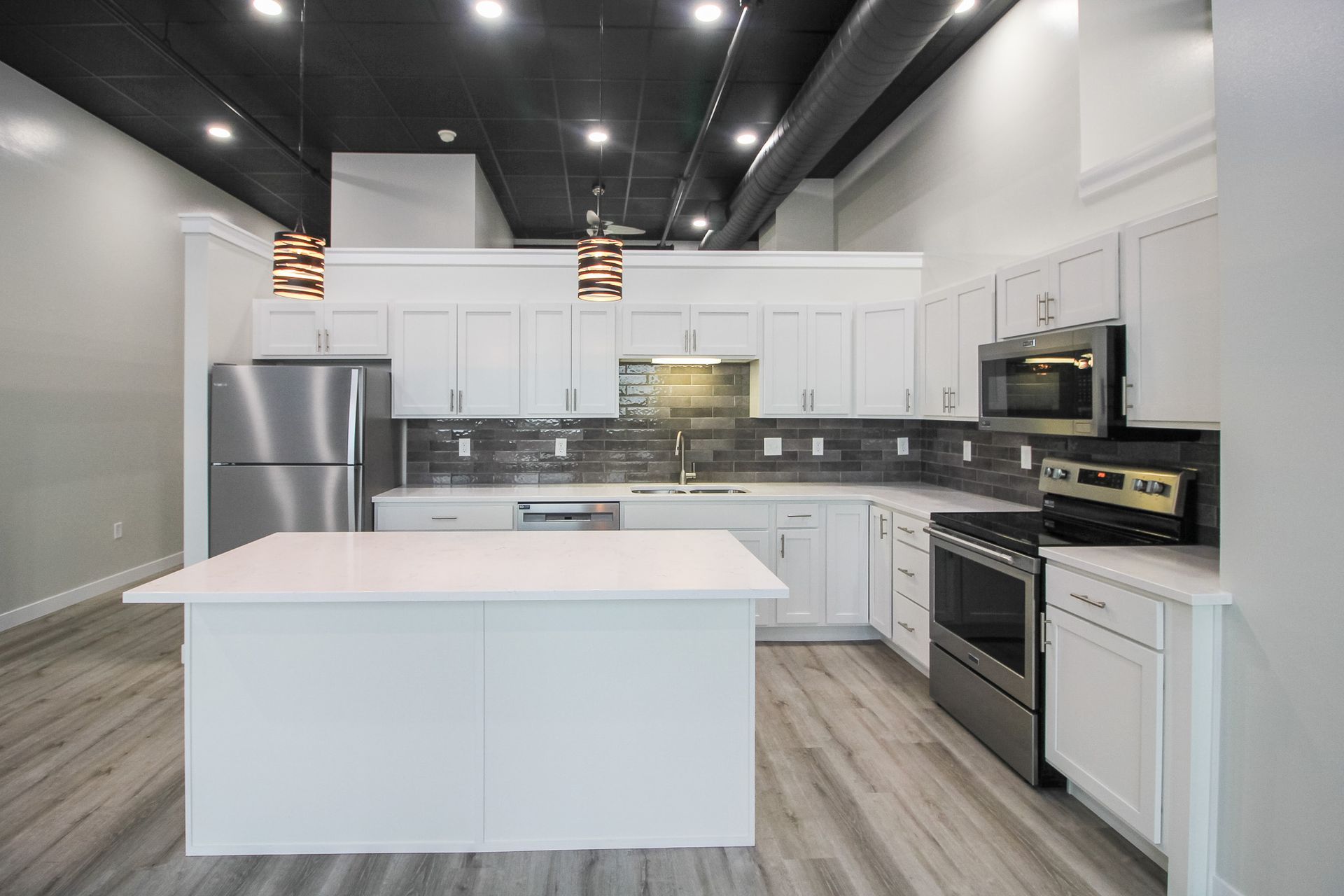 Modern white kitchen with island, stainless steel appliances, and black ceiling lights