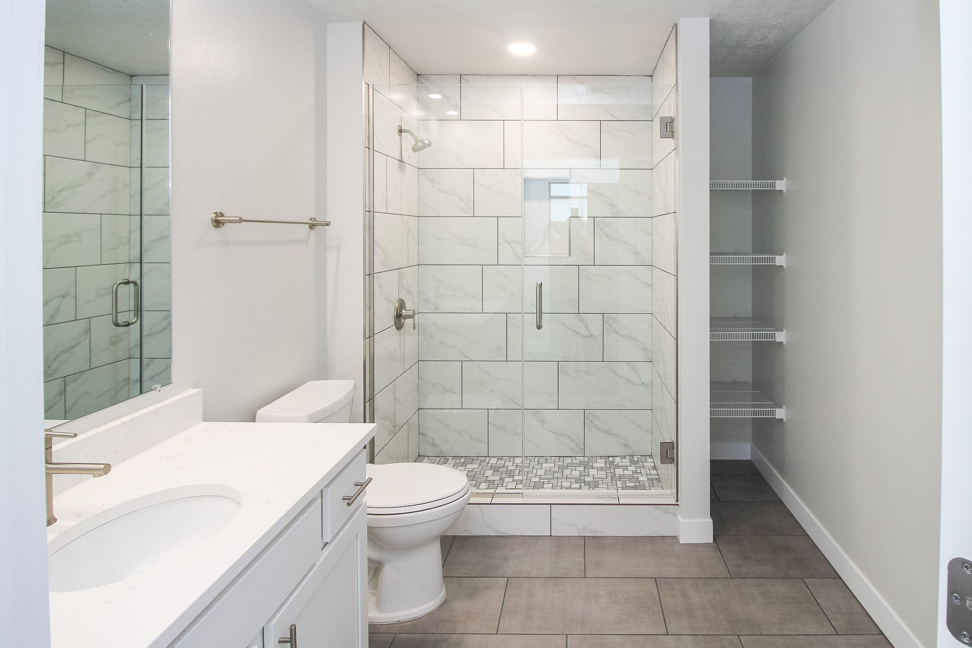 Bright modern bathroom with glass shower, toilet, vanity, and gray tile floor