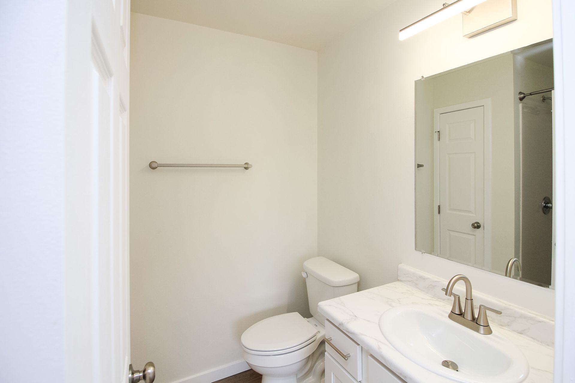 Small white bathroom with toilet, sink, mirror, and towel bar