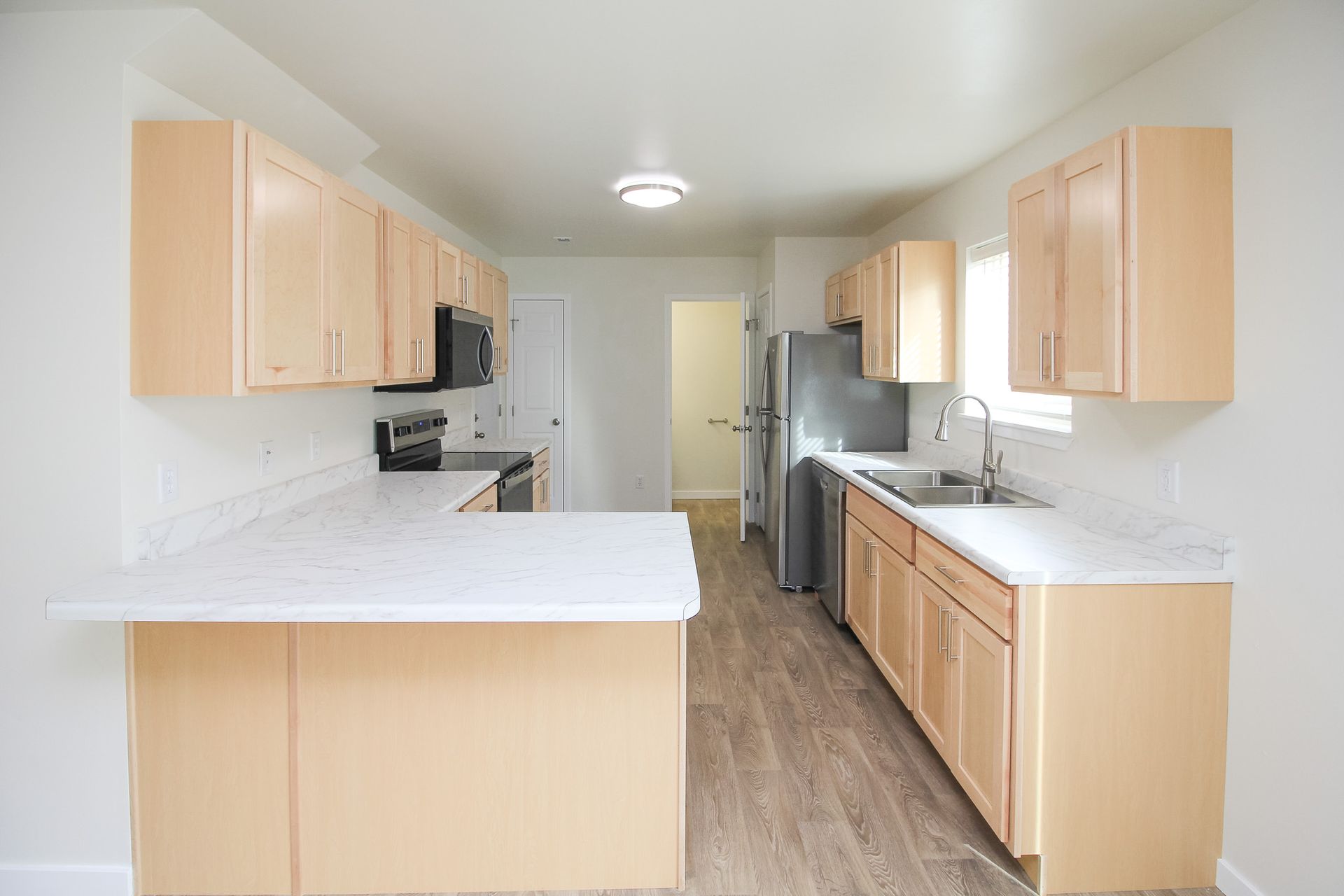 Bright kitchen with light wood cabinets, white countertops, and stainless steel appliances.