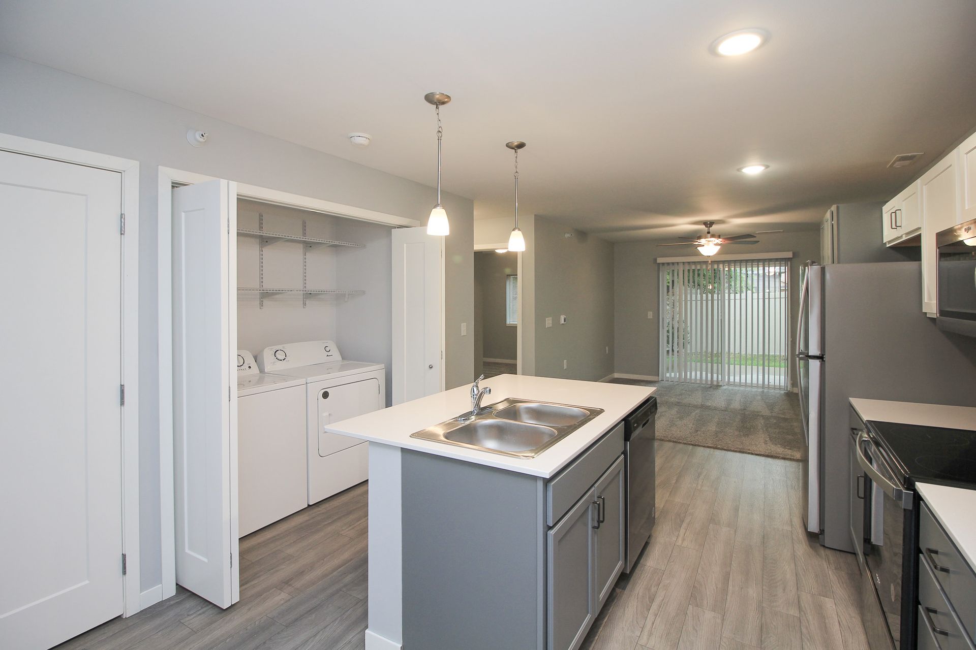 Modern kitchen with gray cabinets, white island, pendant lights, and sliding doors to a bright room