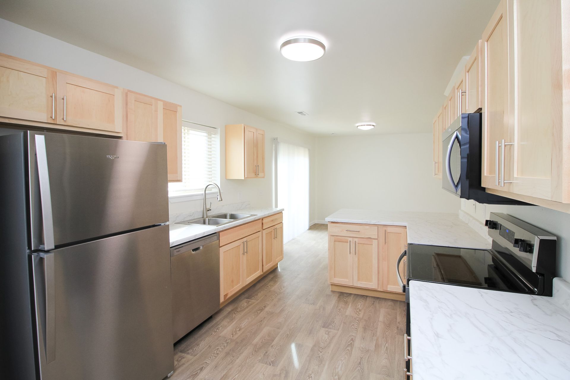 Bright kitchen with light wood cabinets, stainless fridge, white counters, and a small island.