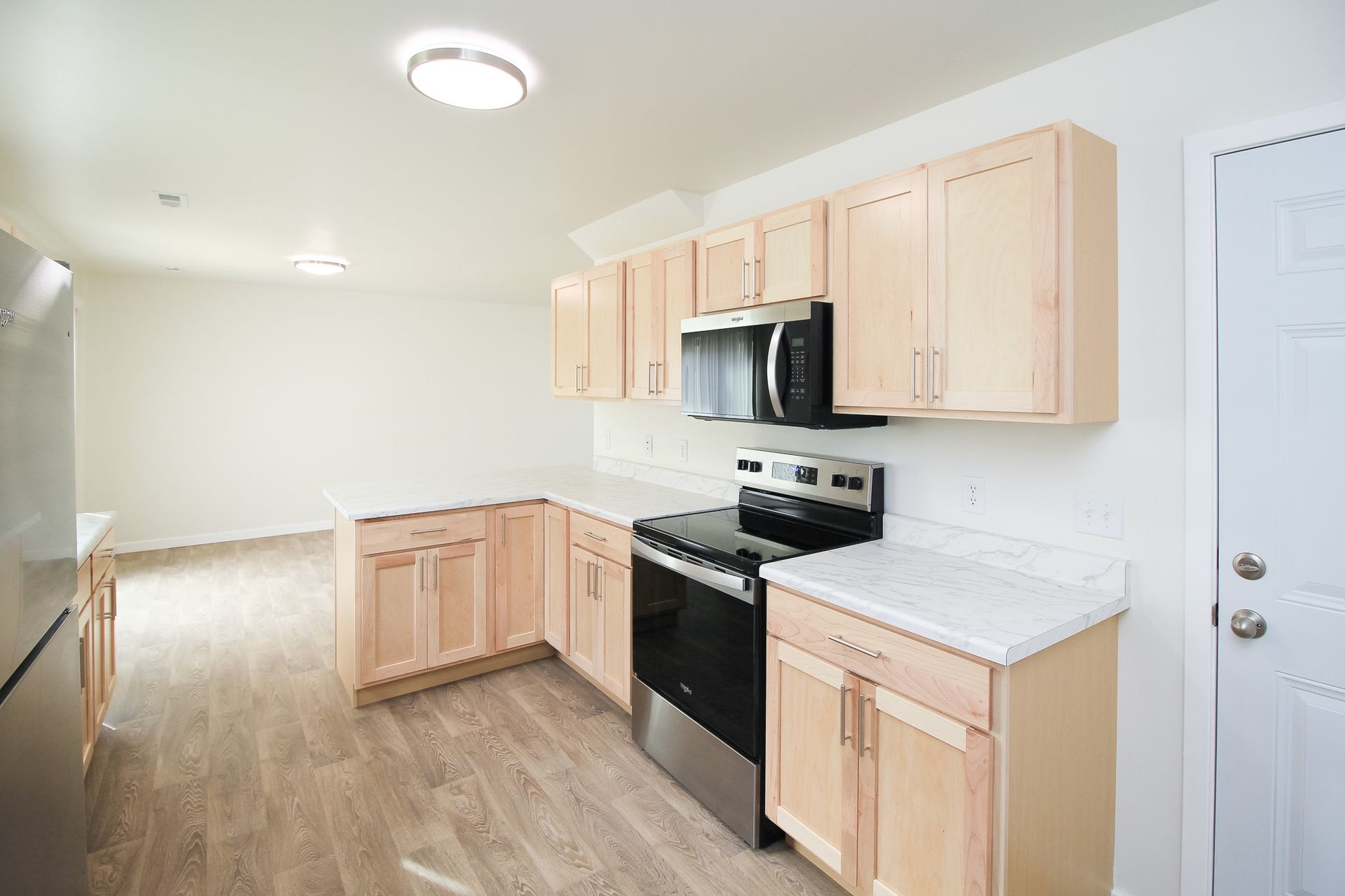 Bright, empty kitchen with light wood cabinets, stainless steel appliances, and white countertops