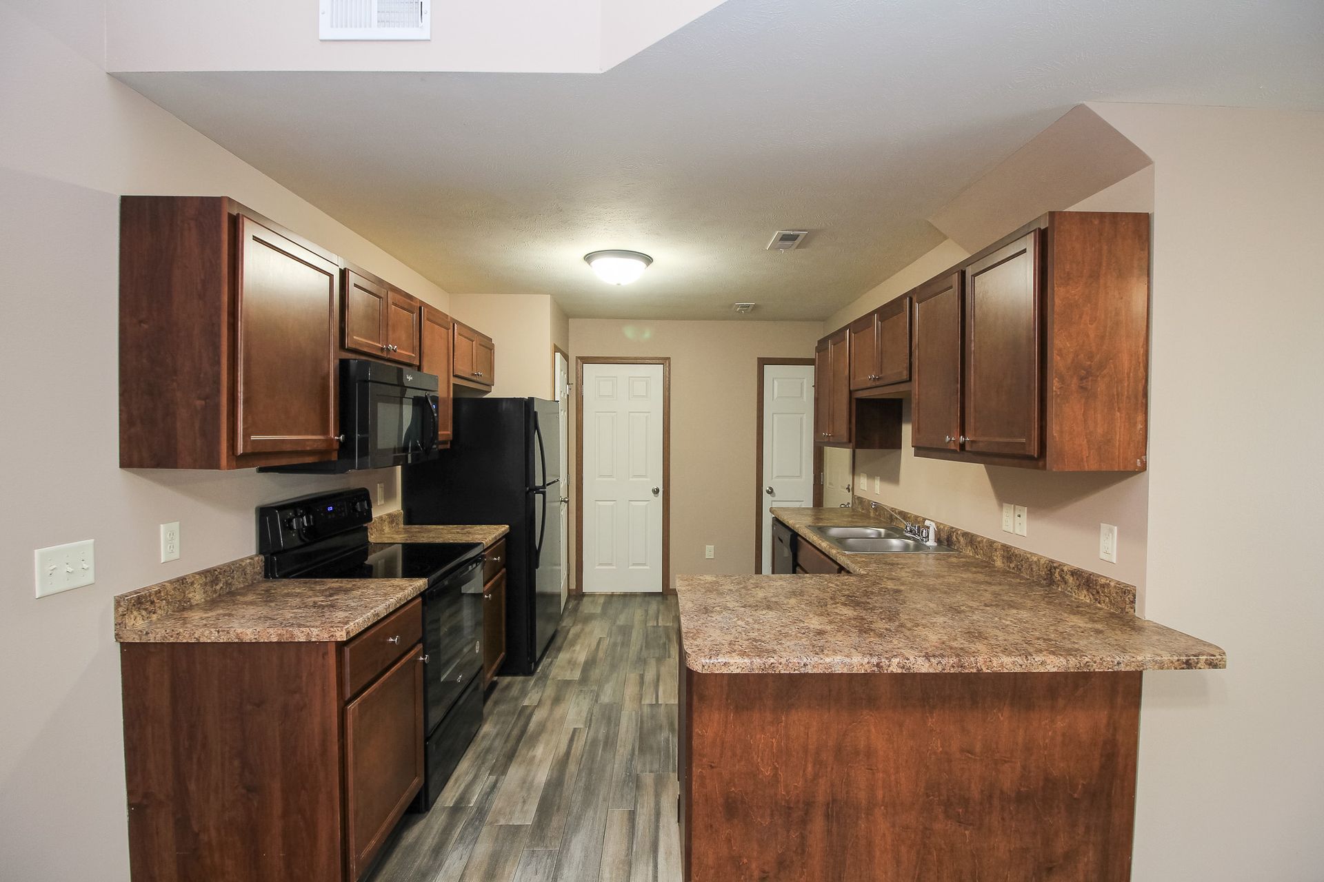 Galley kitchen with dark wood cabinets, granite countertops, black appliances, and light tile flooring