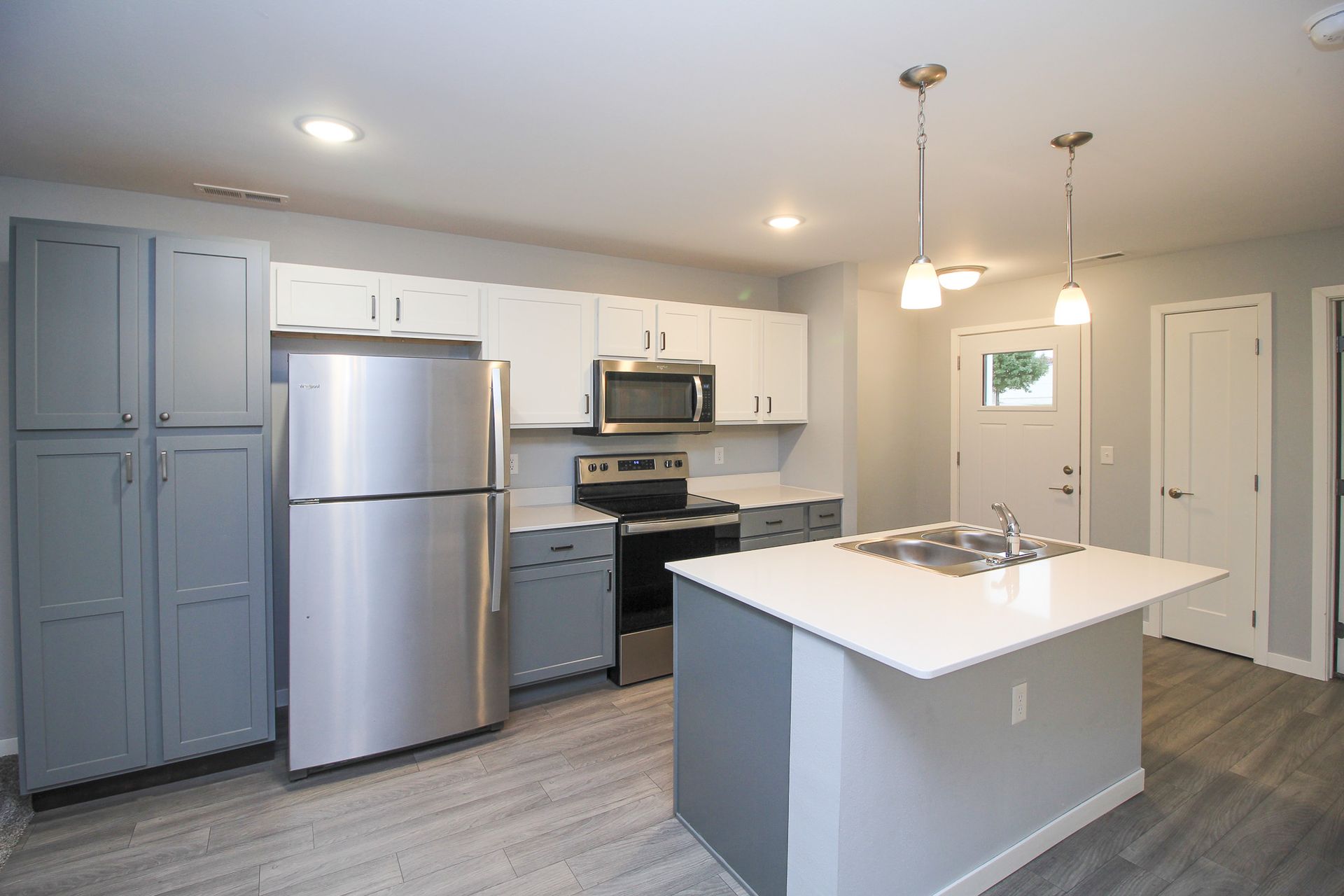 Modern kitchen with stainless steel appliances, white cabinets, and a central island under pendant lights