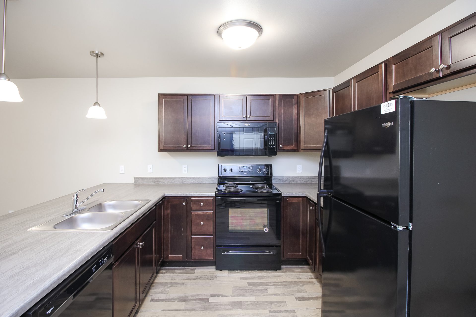 Modern kitchen with dark cabinets, black appliances, light countertops, and an island with sink and pendant lights