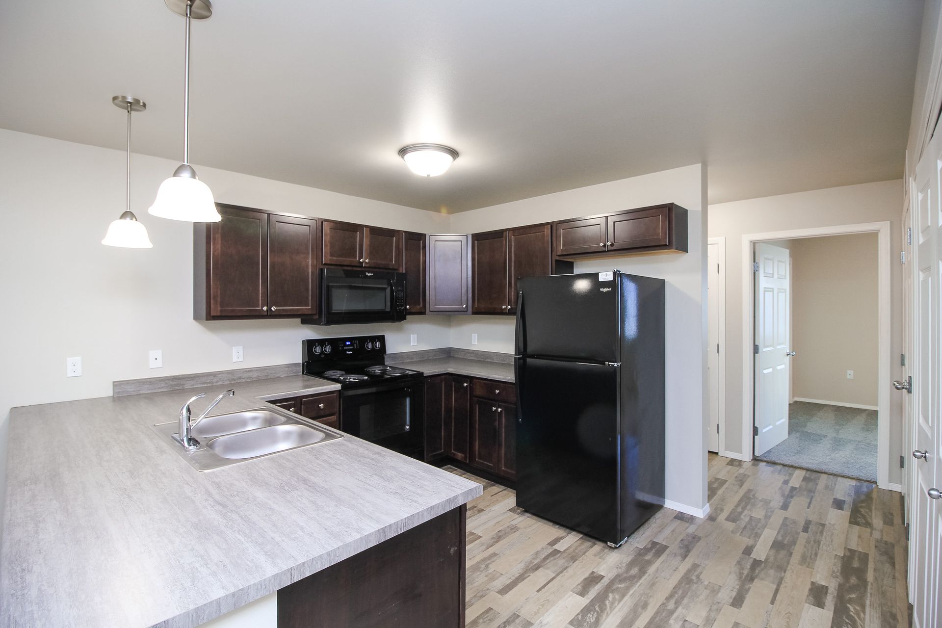 Modern kitchen with dark cabinets, black appliances, light countertops, and pendant lighting
