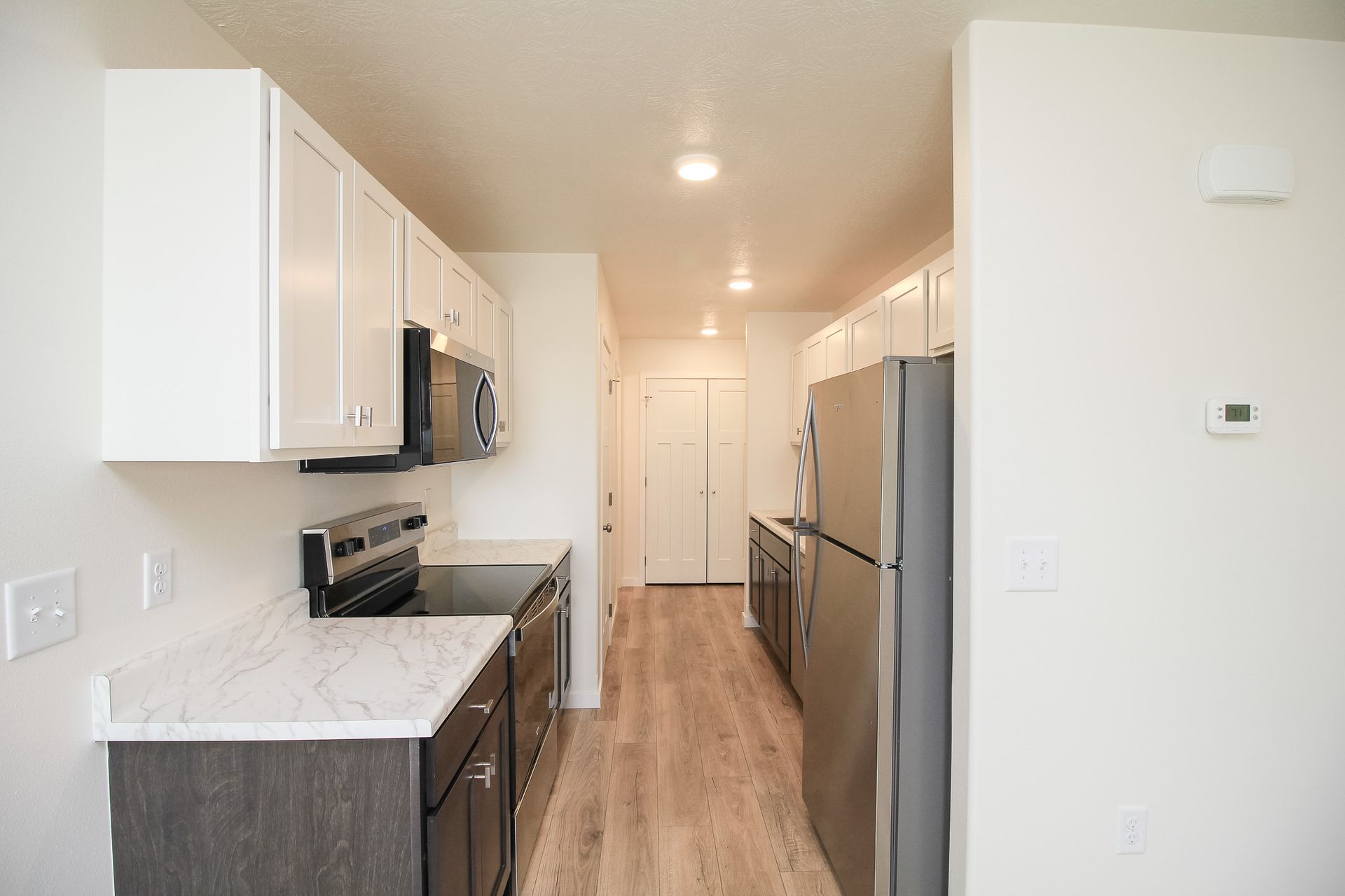 Modern galley kitchen with white cabinets, stainless appliances, and wood flooring