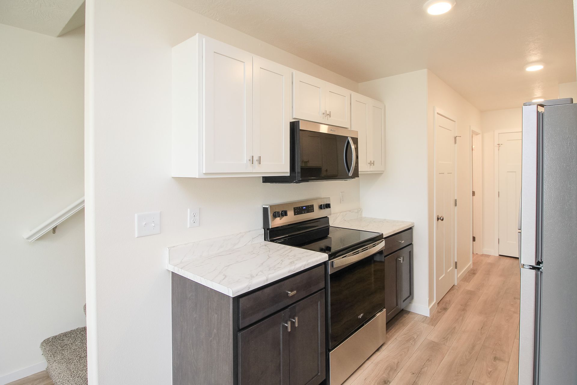 Bright kitchen hallway with white cabinets, black stove, and dark lower cabinets along a light wood floor.