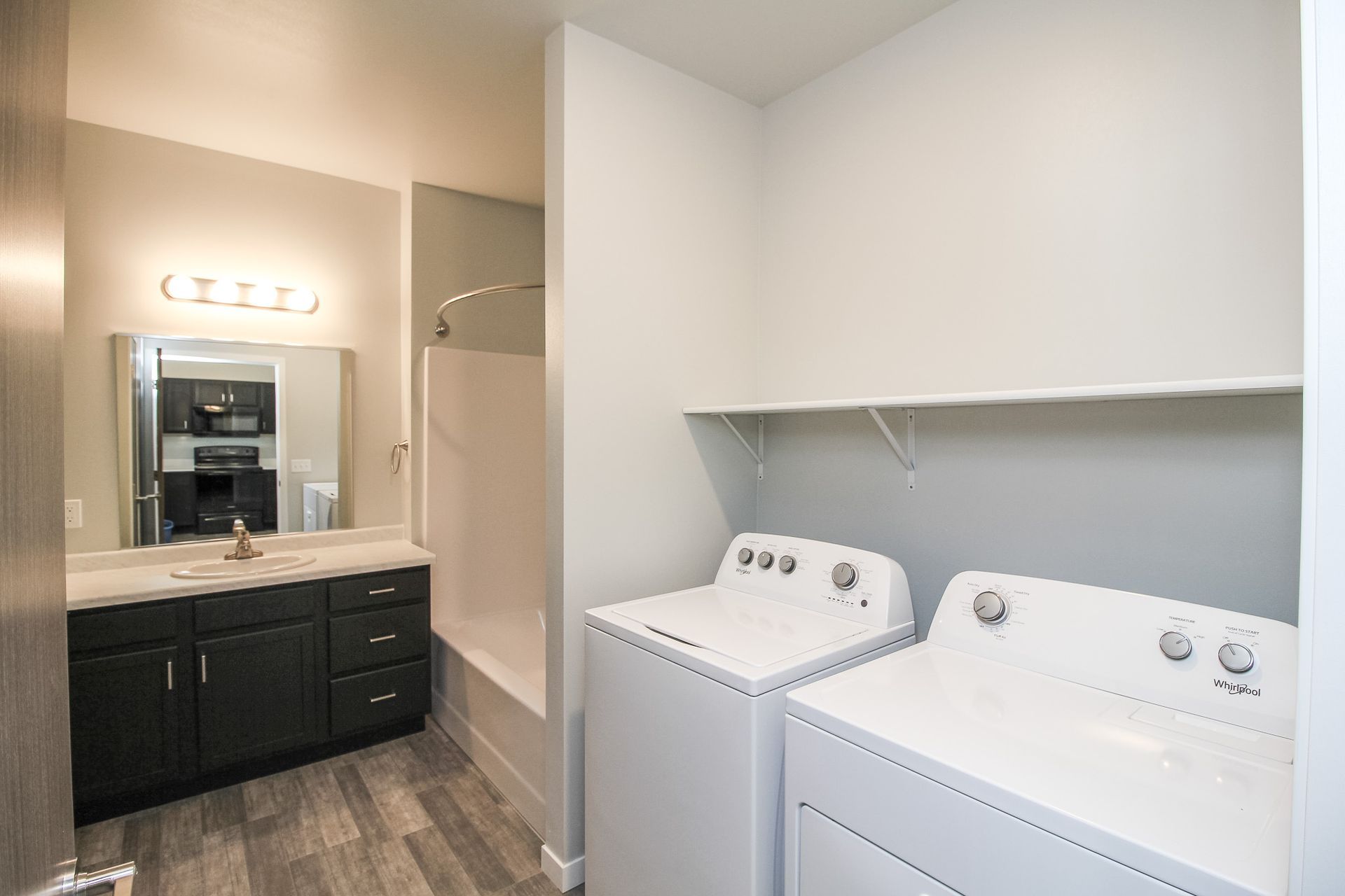 Laundry room with white washer and dryer beside a dark vanity and mirror under bright lighting