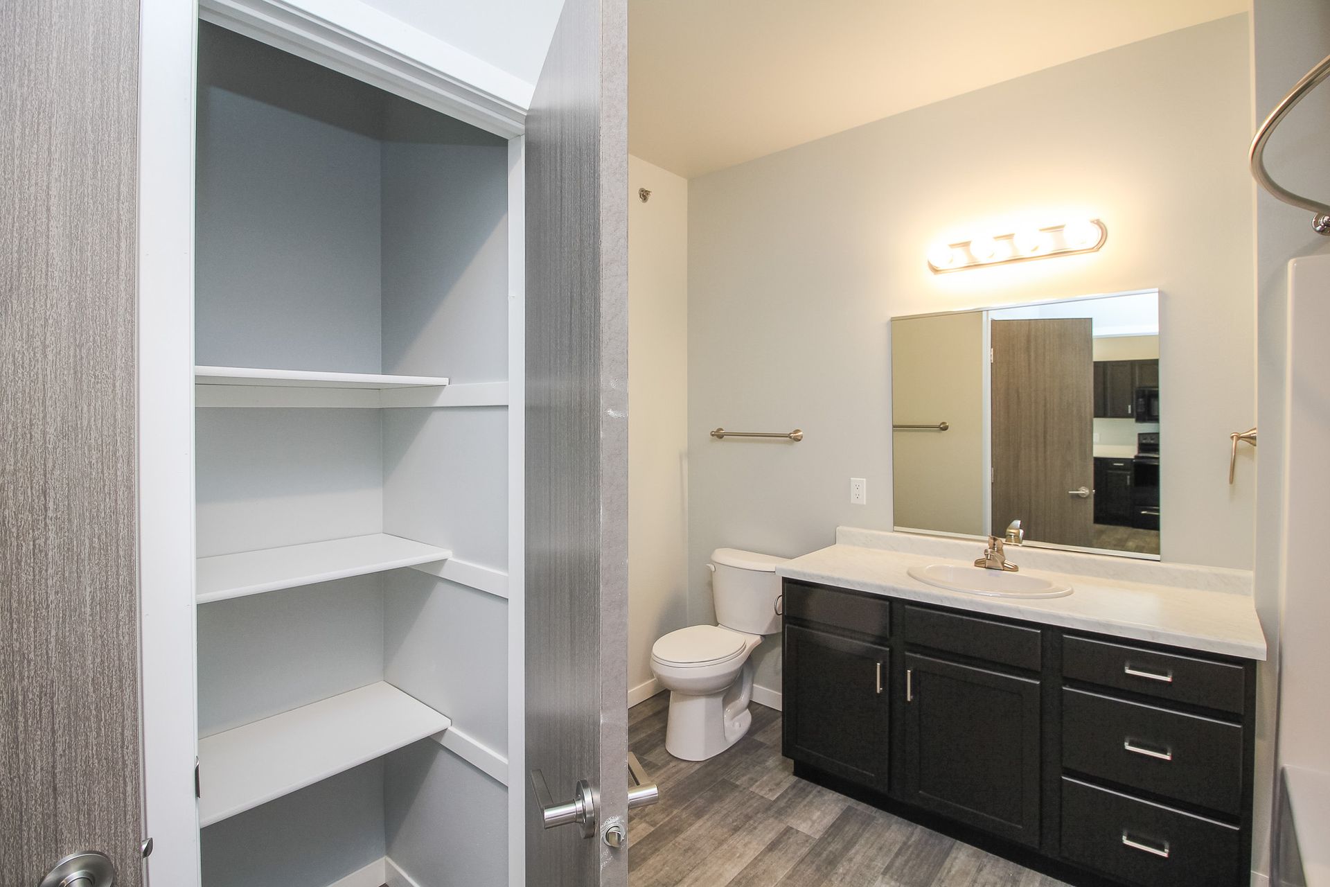 Bathroom with dark vanity, white countertop, mirror, toilet, and open closet shelves.