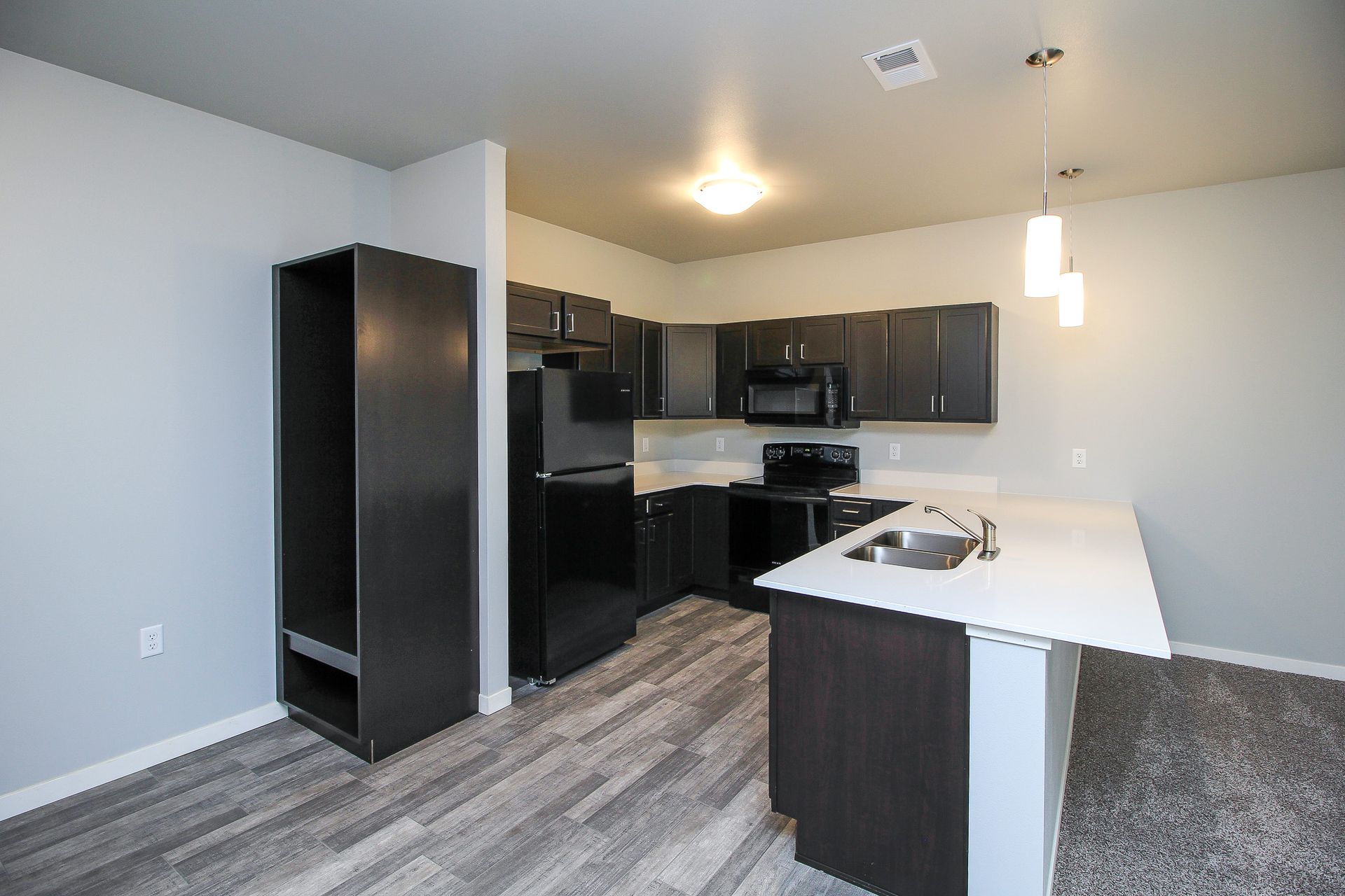 Modern kitchen with dark cabinets, black appliances, white island, and gray wood flooring