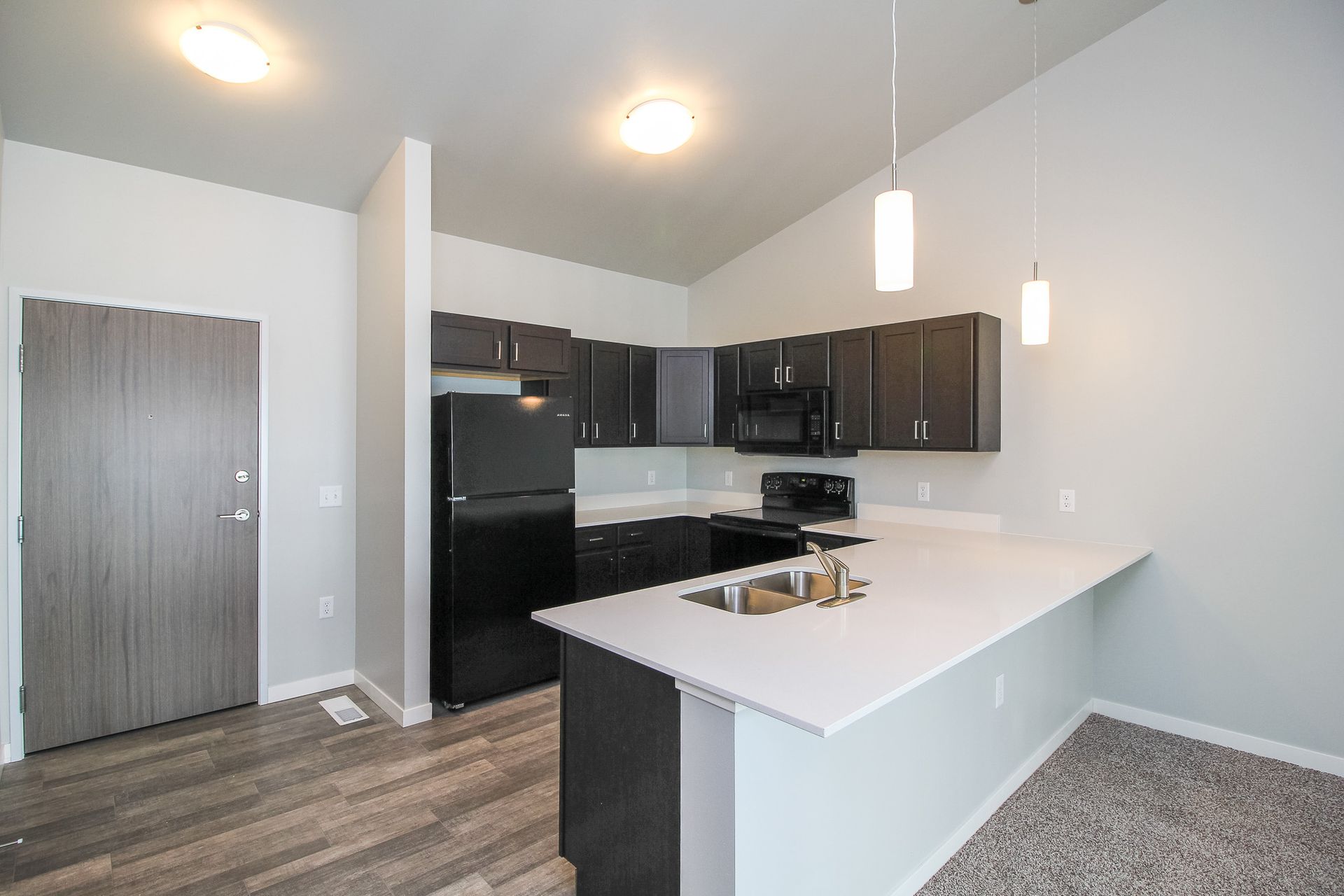 Modern apartment kitchen with dark cabinets, black appliances, white island, and gray wood flooring